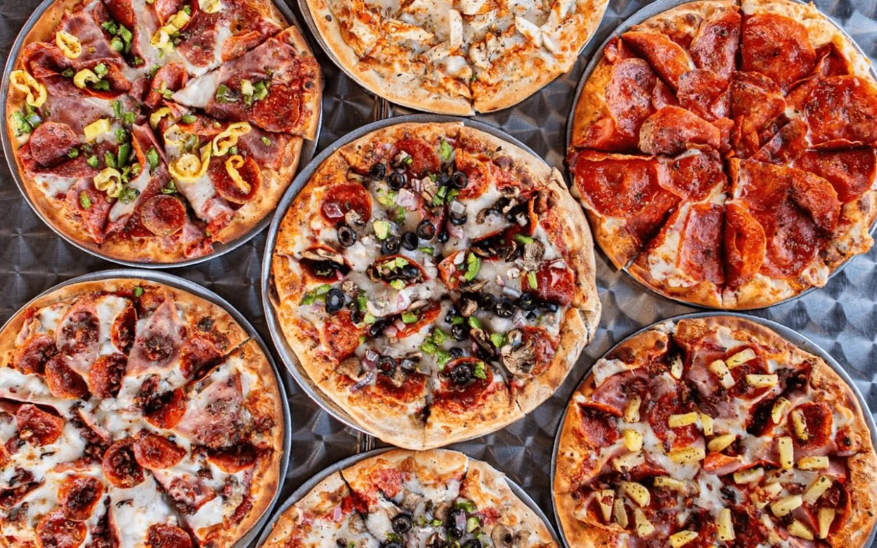 An assortment of pizzas arranged on a table, showcasing different toppings, including pepperoni, vegetables, and cheese.