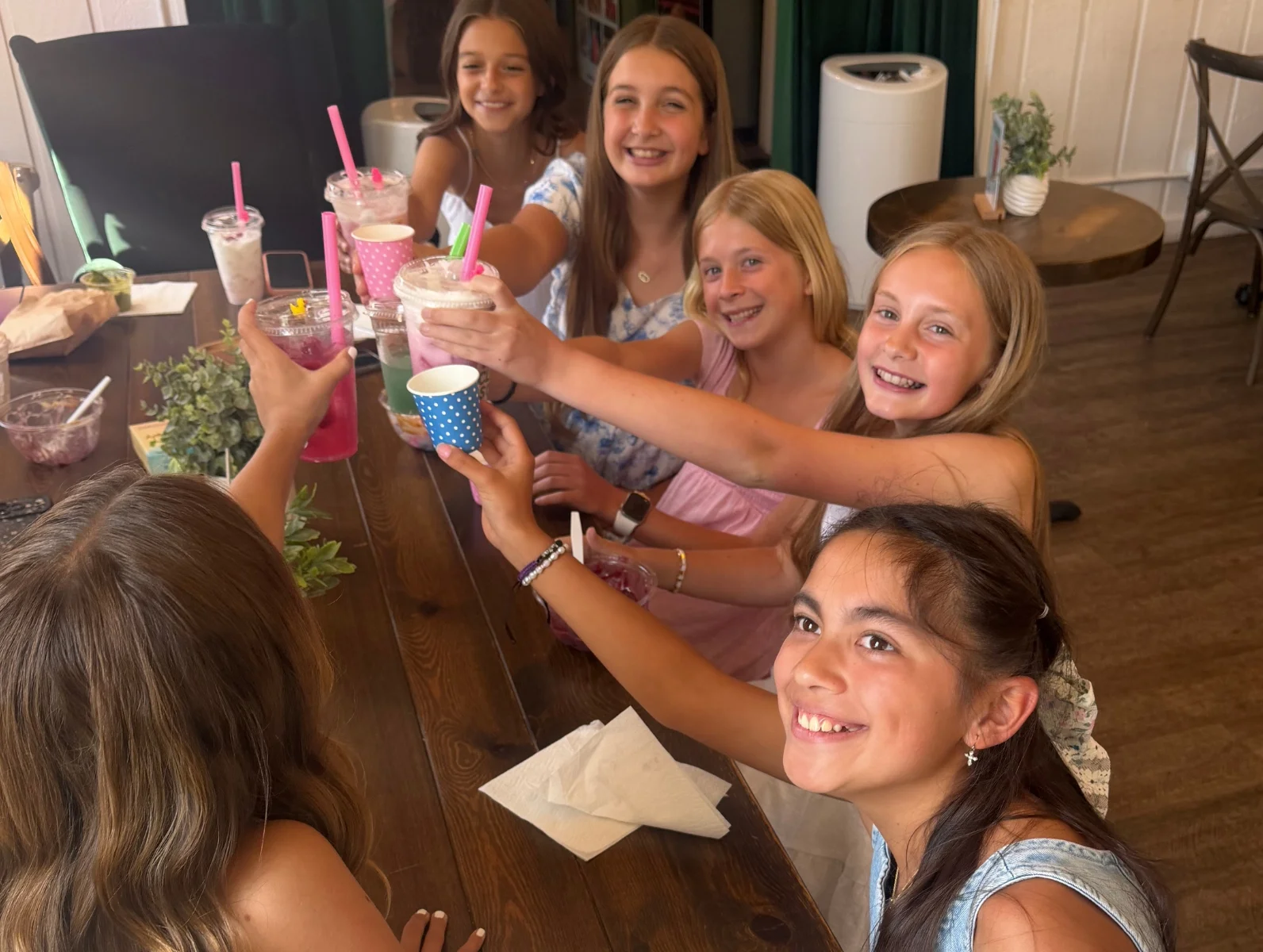 Group of girls toasting with colorful drinks in a cozy cafe