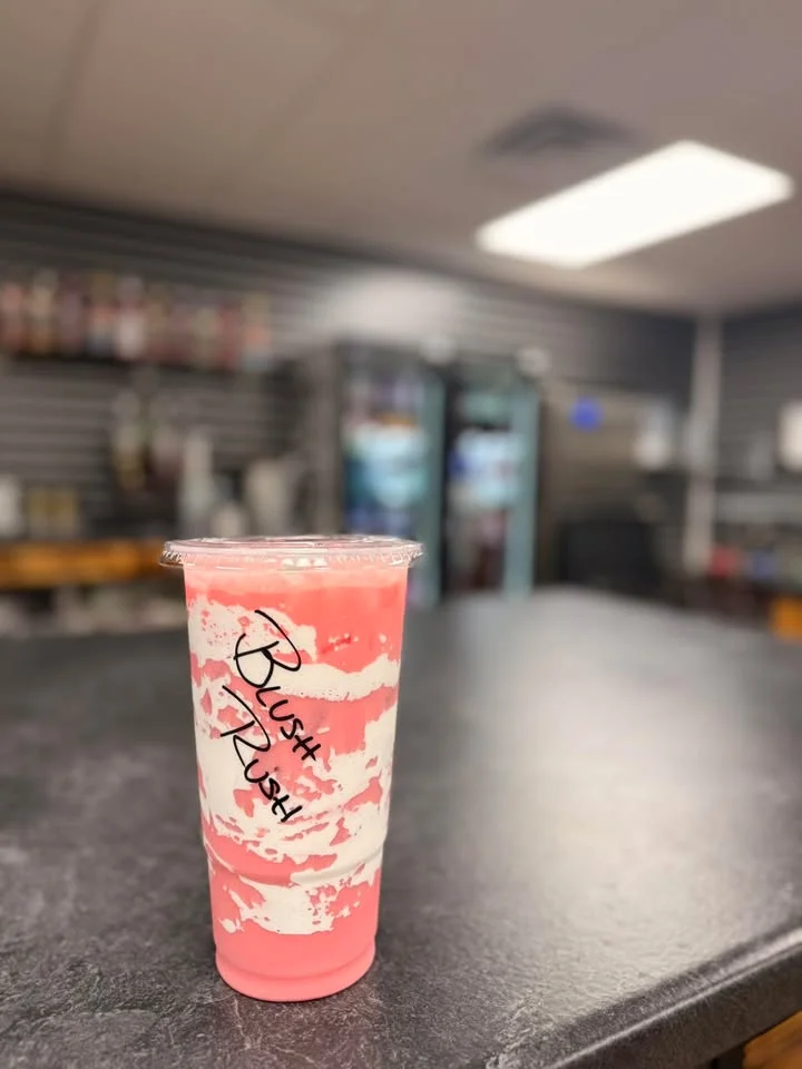 A striped pink and white drink in a clear cup, sitting on a dark countertop with a blurred backdrop.
