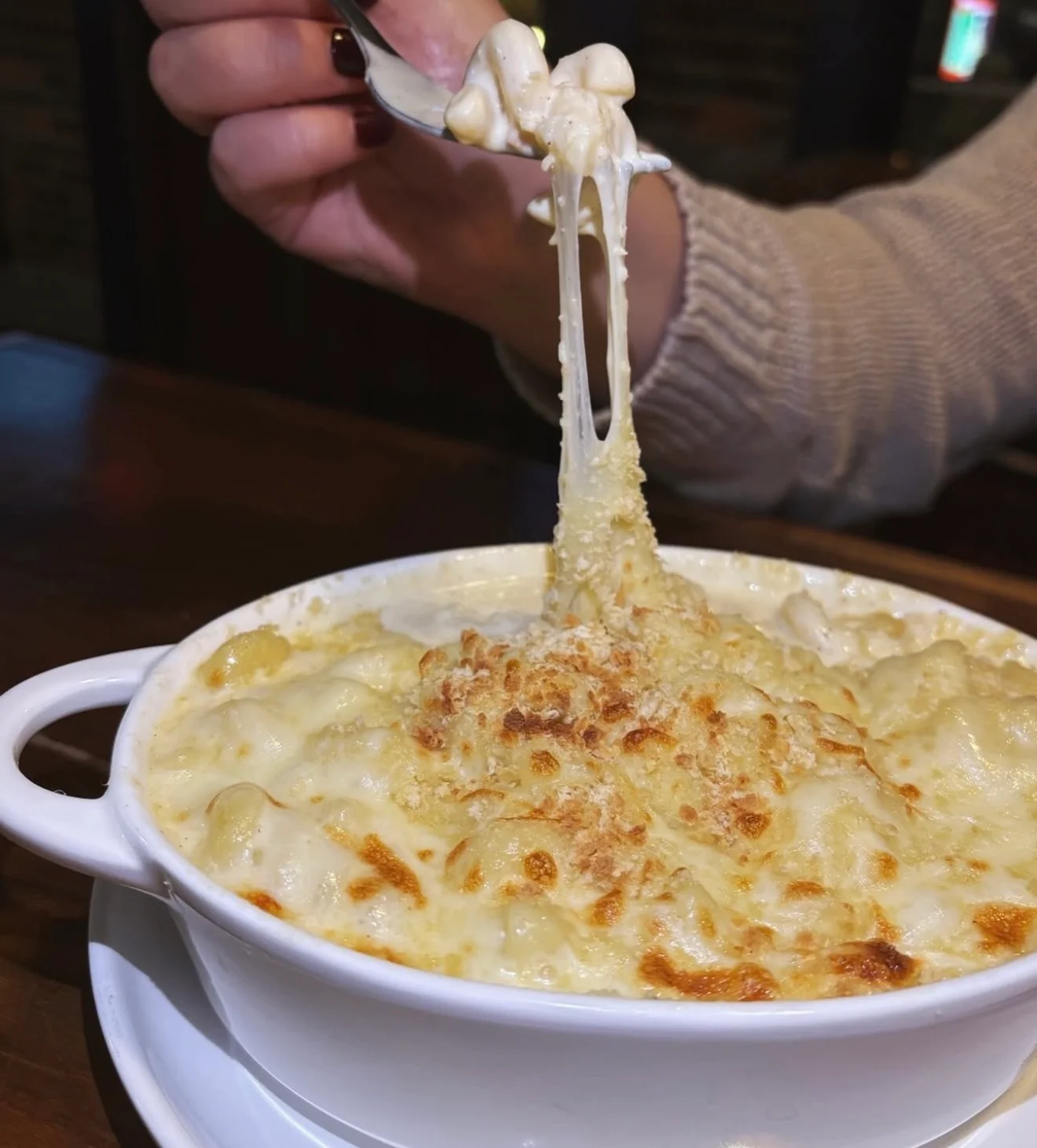 A creamy mac and cheese dish served in a white bowl, featuring melted cheese stretching from a fork.