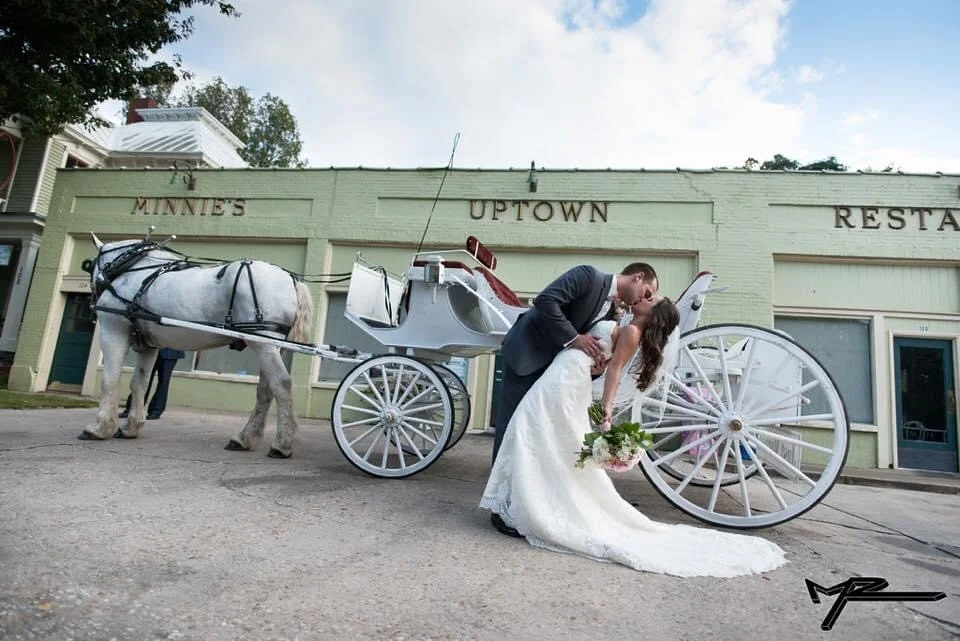Bride and groom kissing by a horse-drawn carriage outside a restaurant