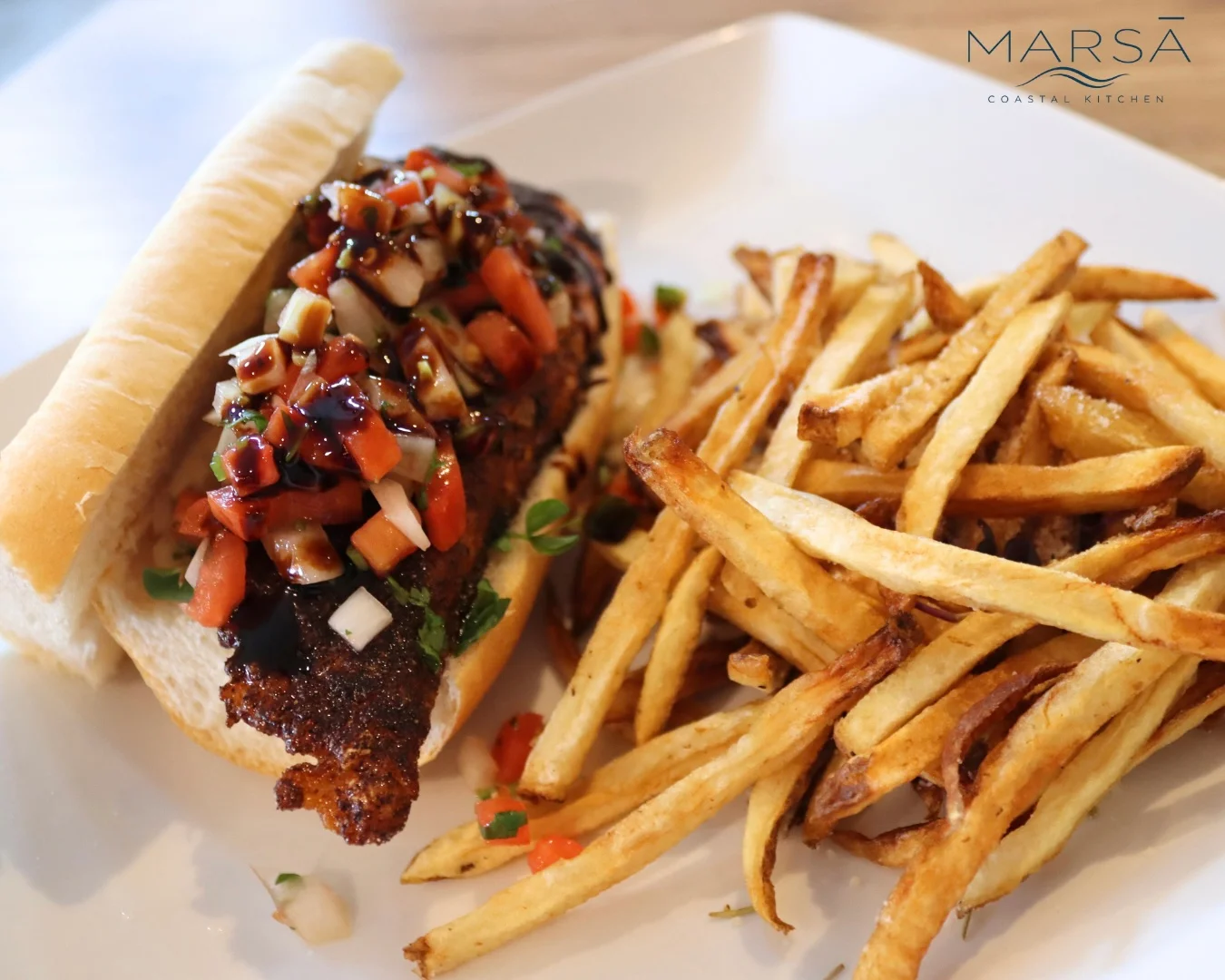 A sandwich featuring a seasoned fillet topped with salsa and herbs, served alongside crispy French fries.