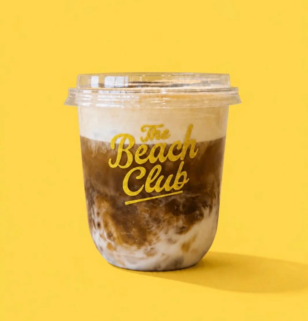 A coffee drink layered with milk and topped with froth in a clear cup, set against a bright yellow background featuring large text promoting rewards.