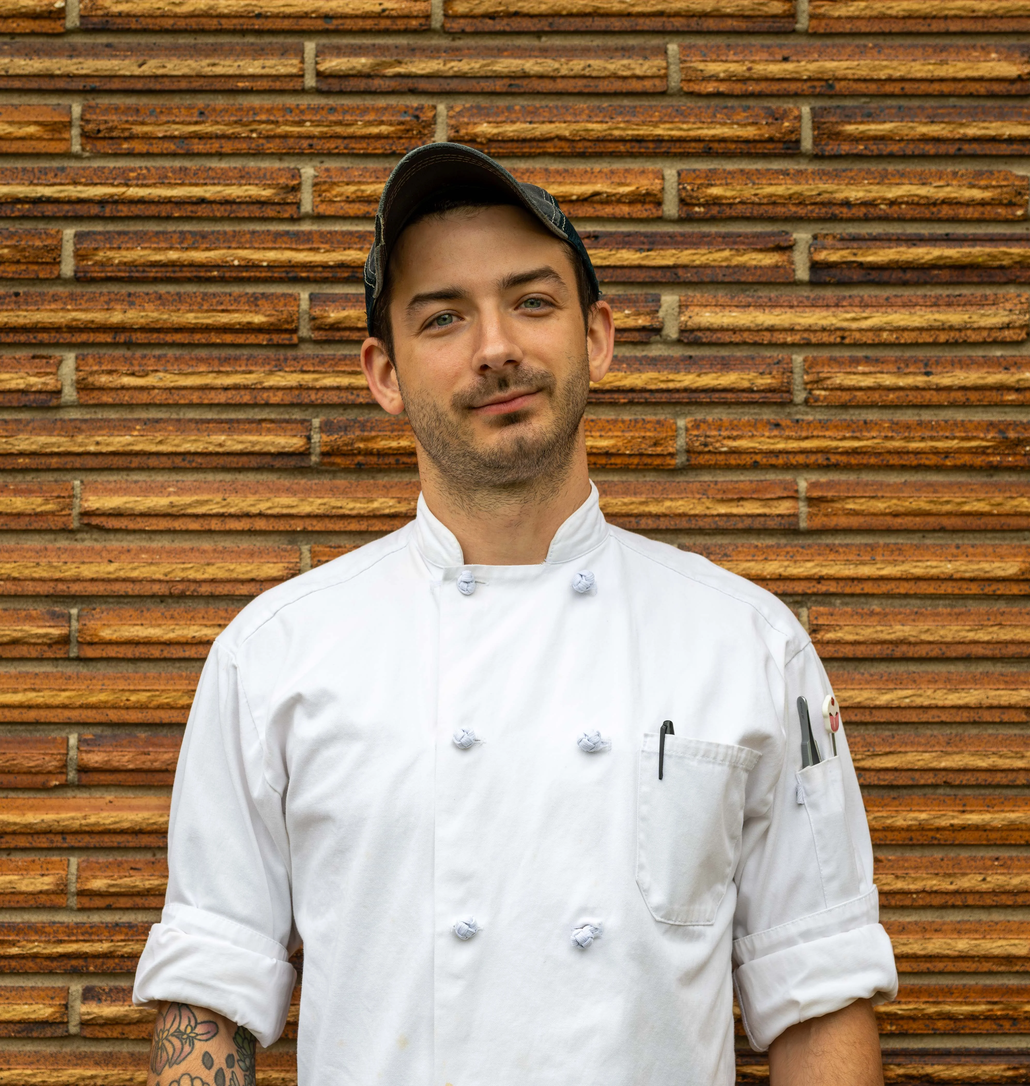 Chef in a white coat posing against a textured brick wall