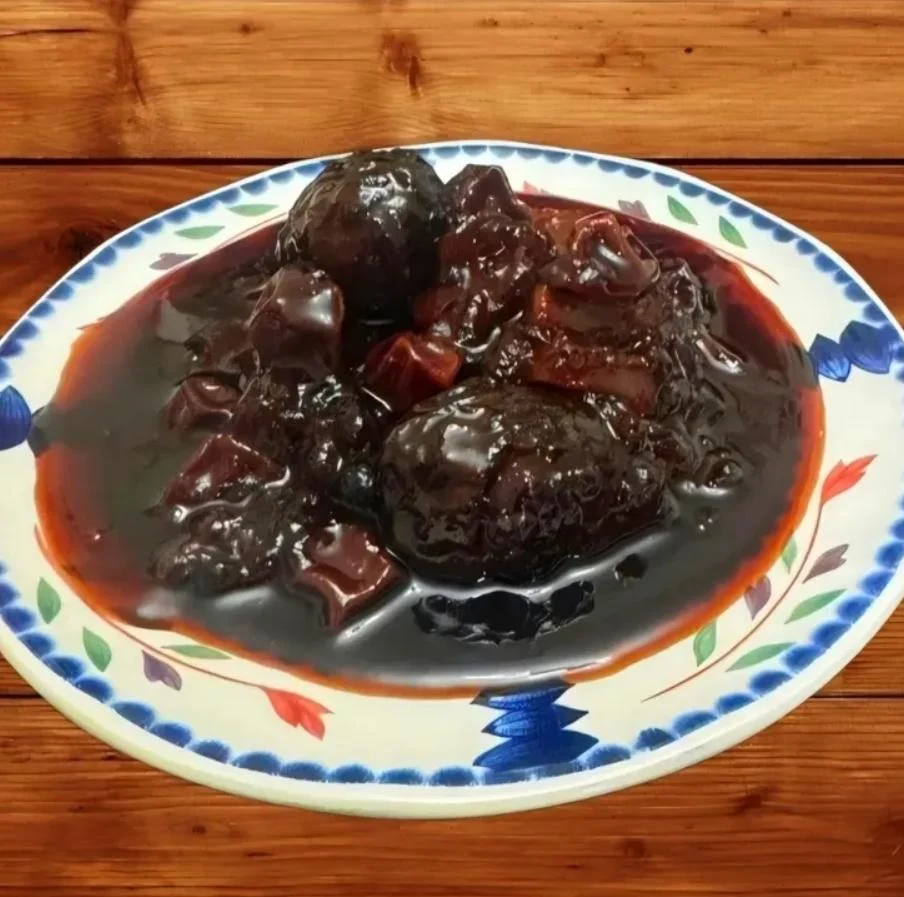 A dish featuring dark, glossy sauce with two round shapes and diced pieces, served on a decorative plate.