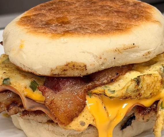 Breakfast sandwich with egg, cheese, and ham on a toasted English muffin.