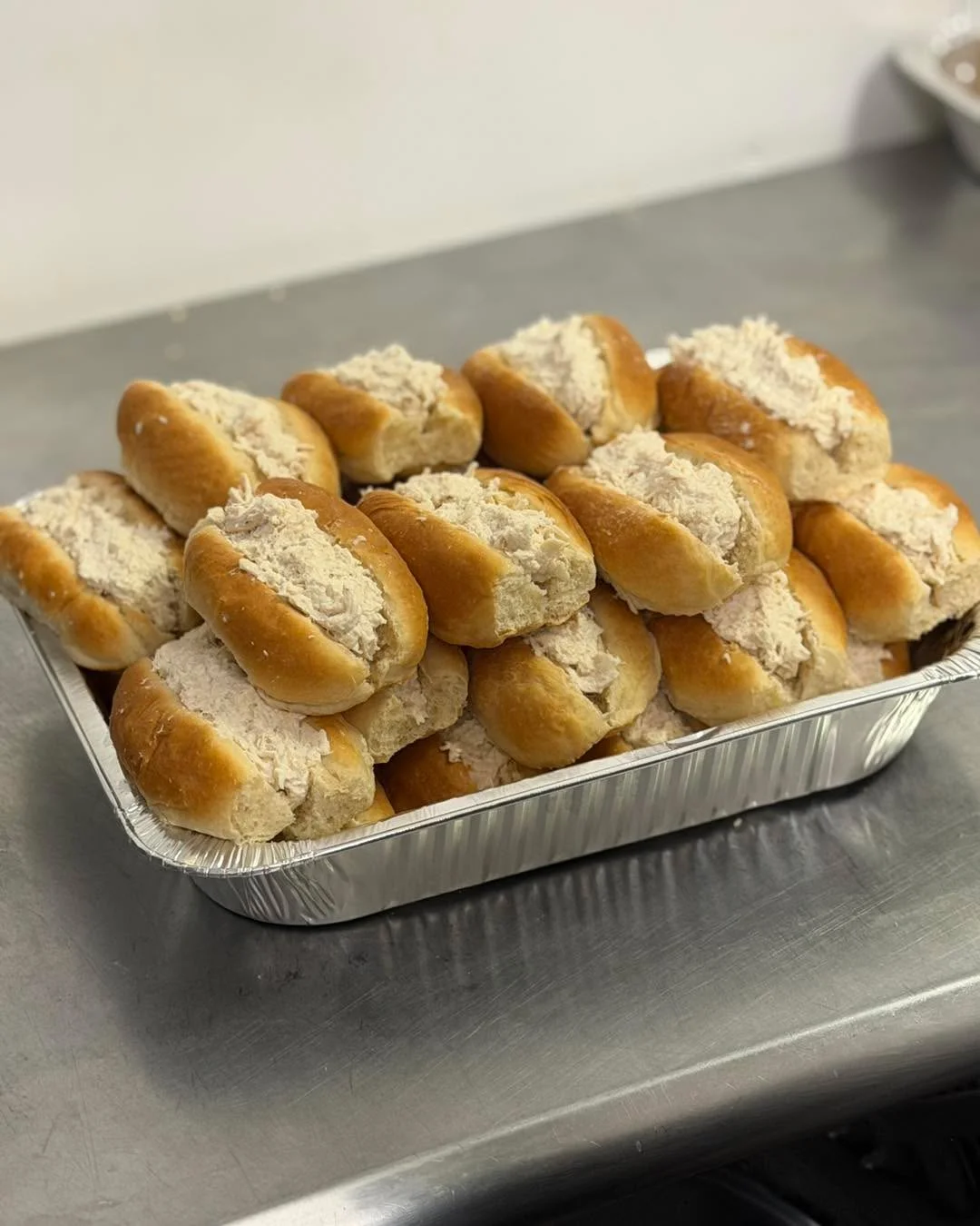 A tray of sandwich rolls filled with a creamy chicken salad mixture, perfectly laid out for serving.