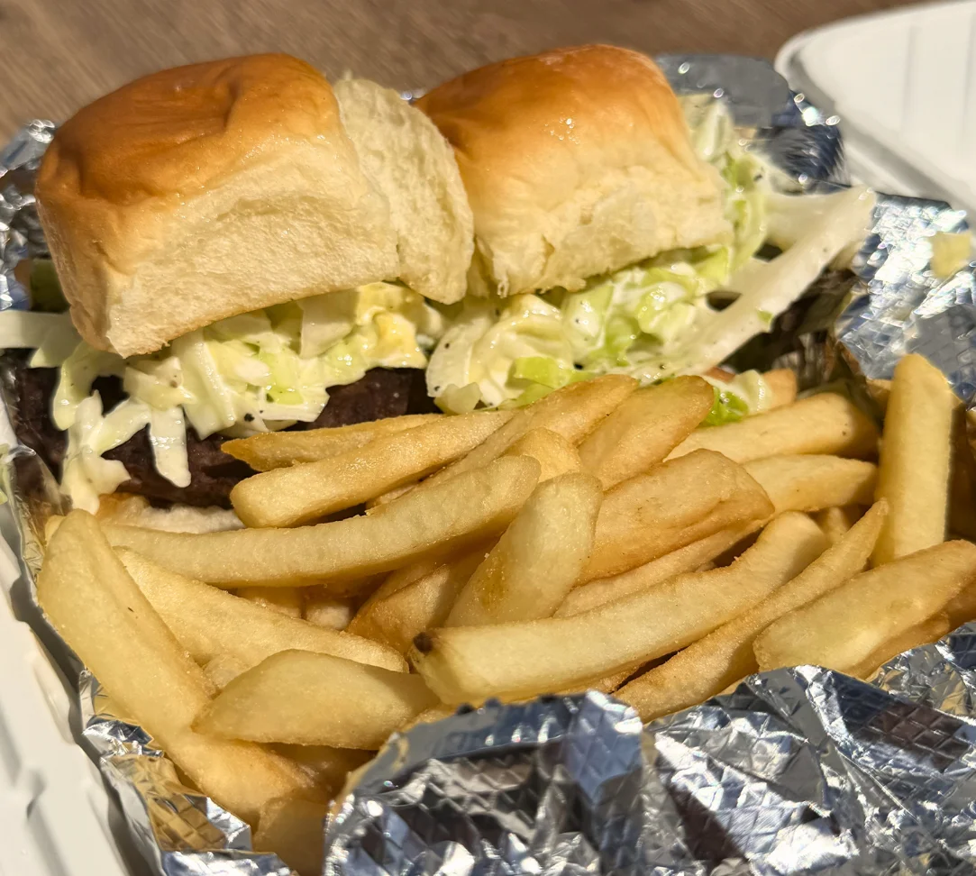 Two sliders with coleslaw and fries in a foil container.