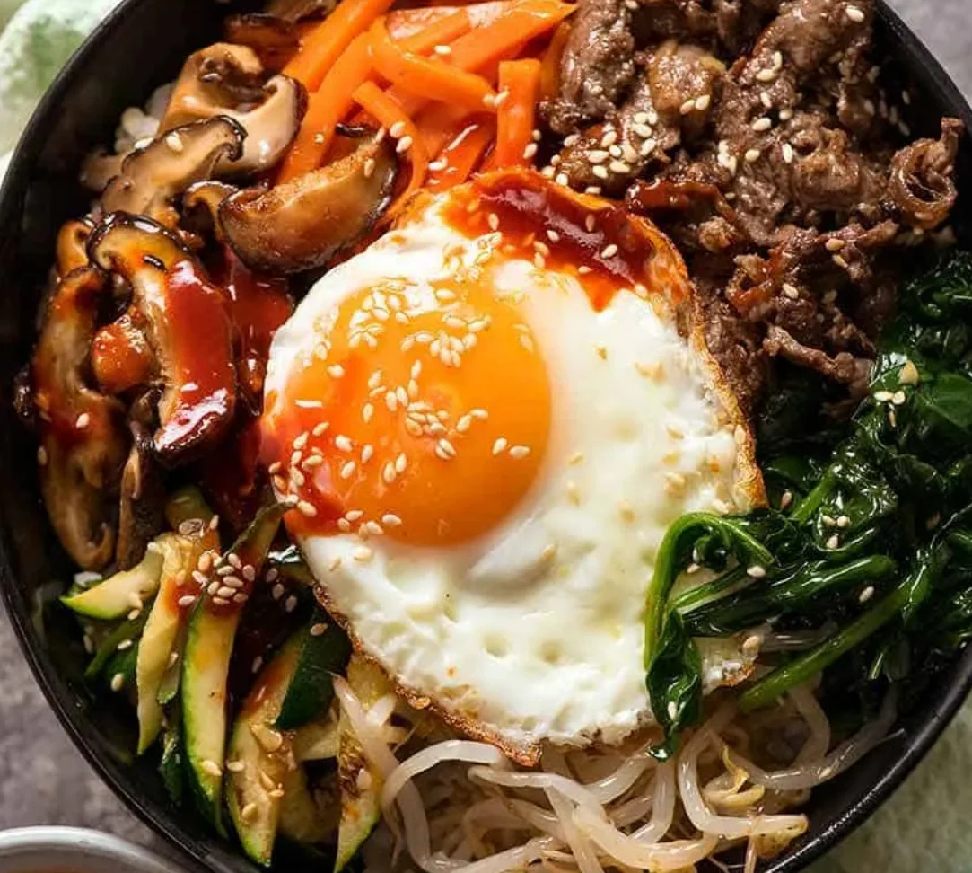 A colorful bowl of bibimbap with vegetables, beef, and a fried egg.