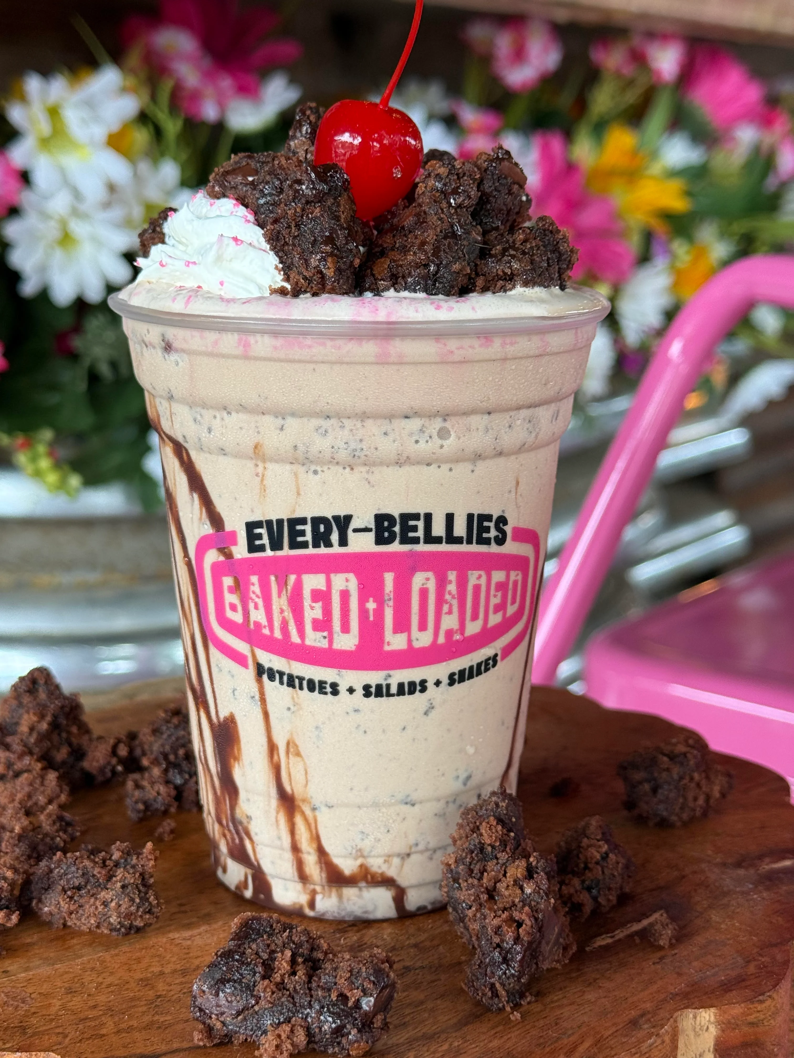 A delicious looking milkshake topped with brownie pieces and a cherry, set against a backdrop of flowers.