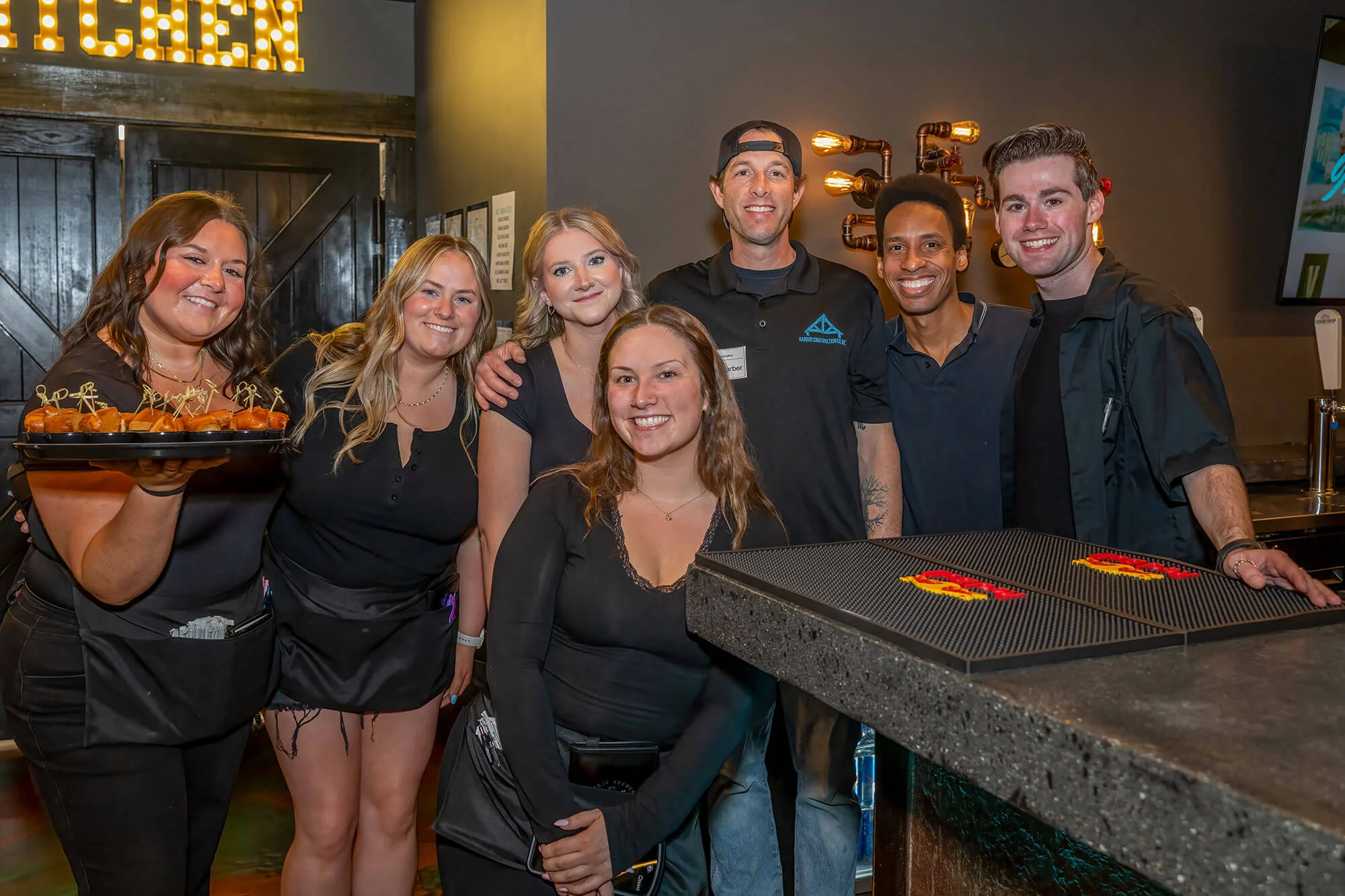 Friendly restaurant staff posing with appetizers in a modern bar setting