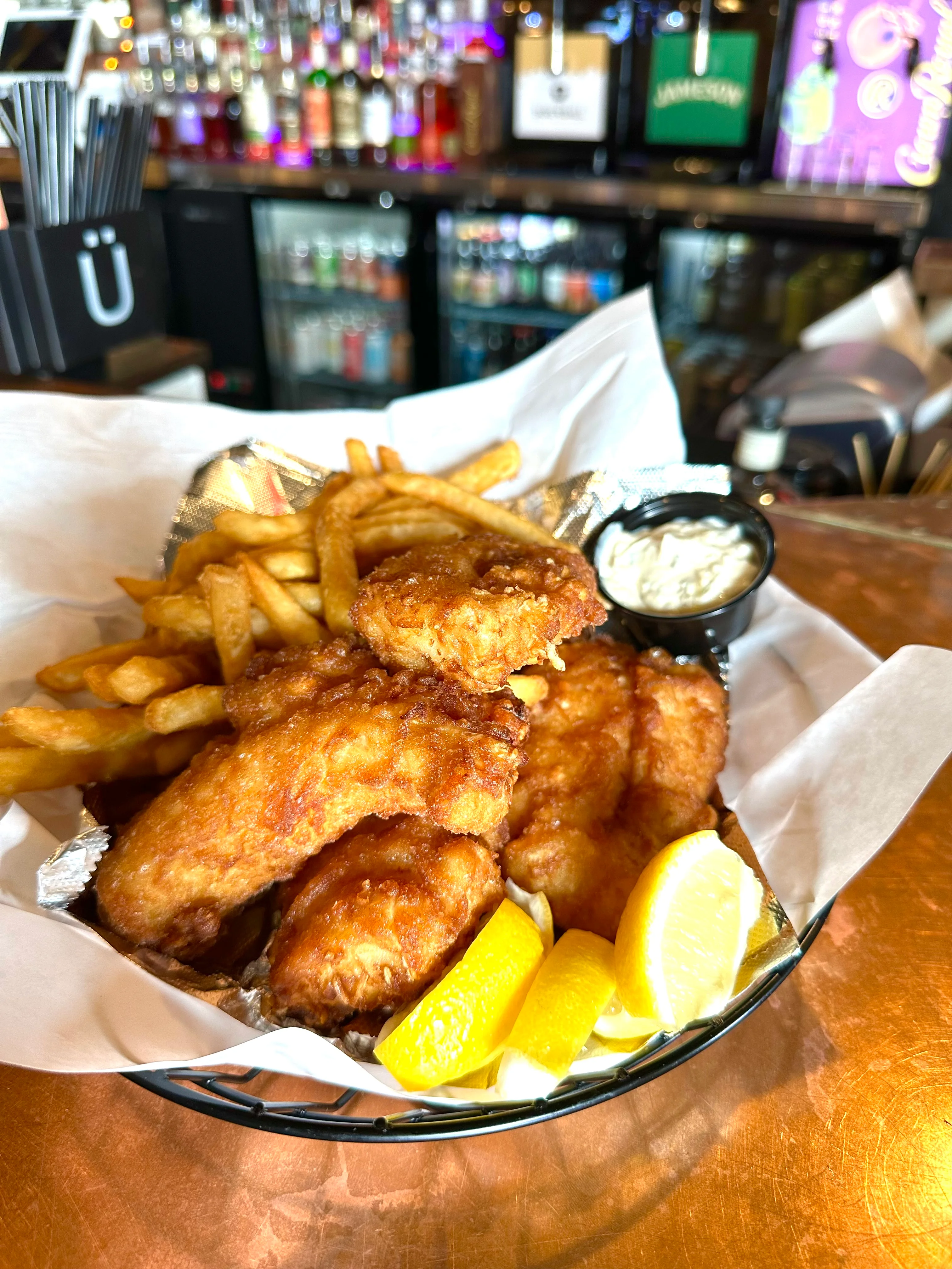 A basket featuring fried chicken, golden fries, and a side of dipping sauce, garnished with lemon wedges.