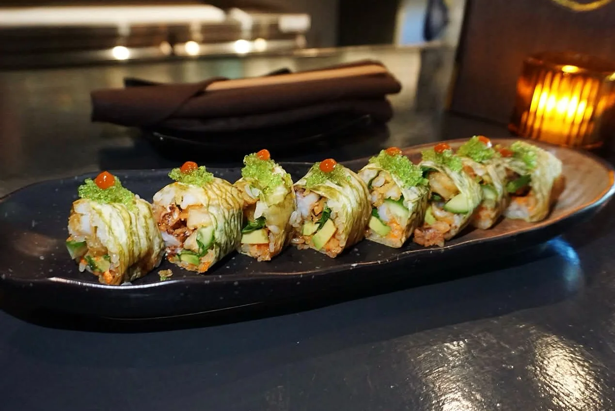 A plate of sushi rolls garnished with green toppings and orange caviar.