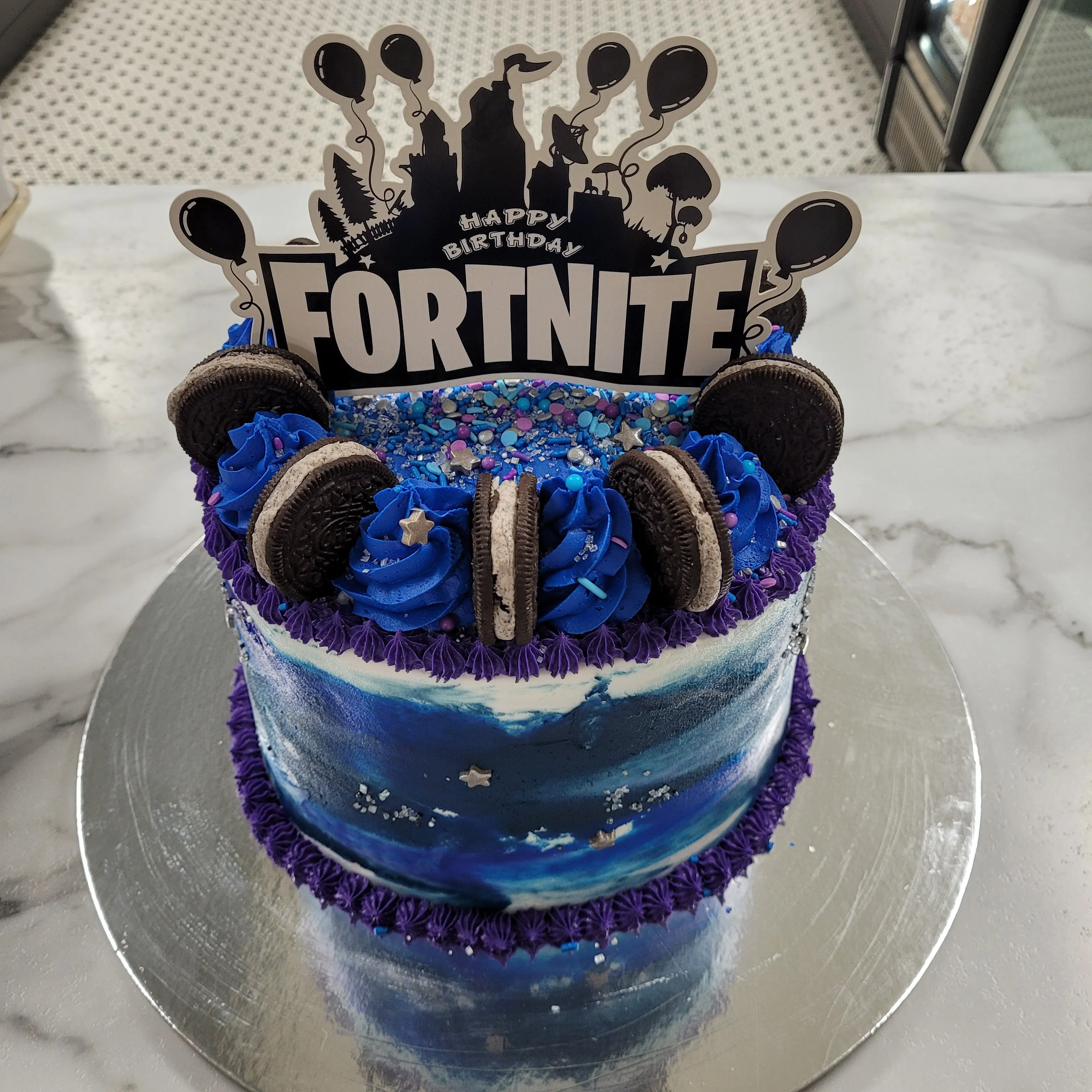 Colorful Fortnite-themed birthday cake with blue frosting and Oreo cookies