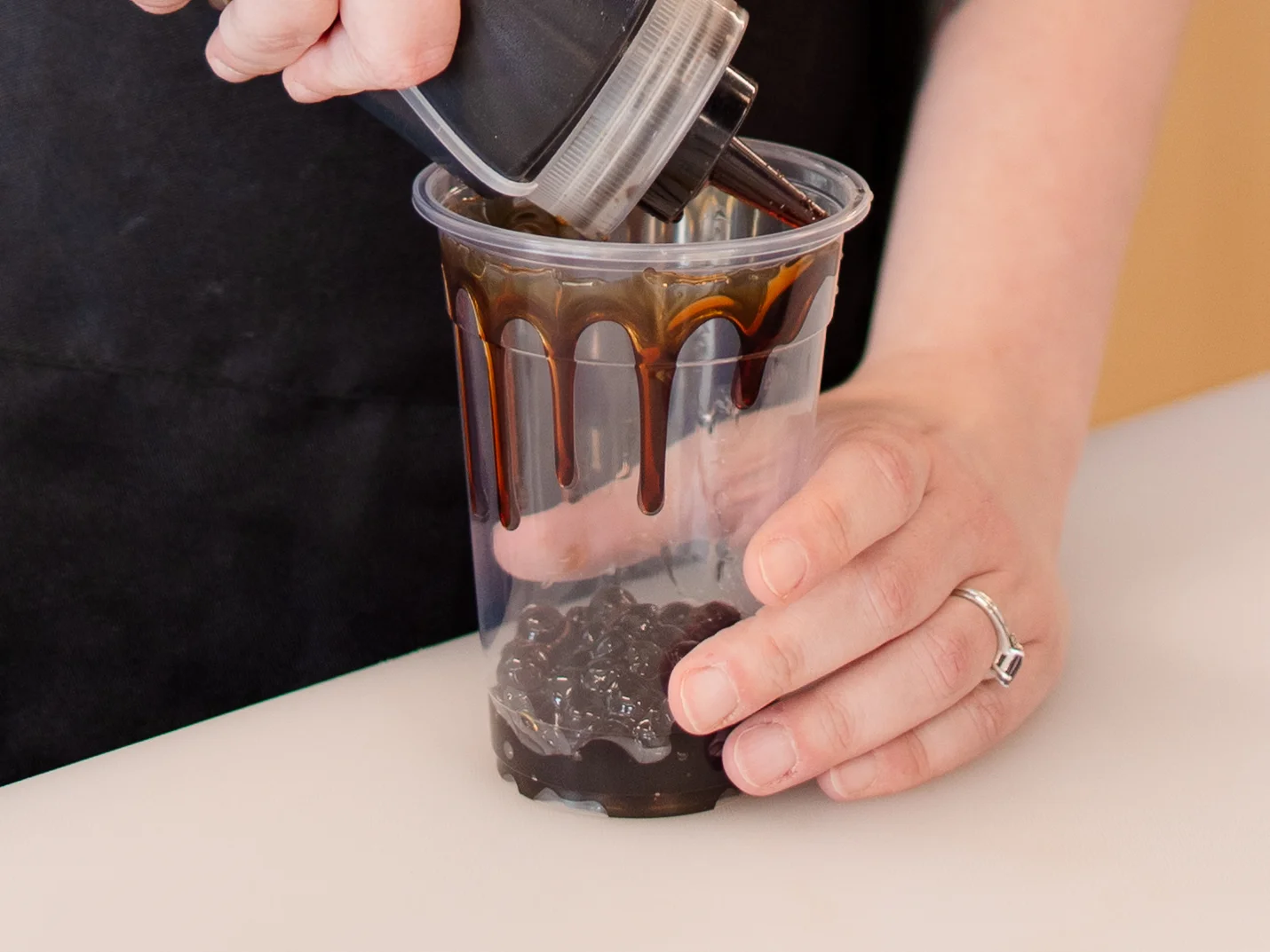 A layered drink in a transparent cup featuring green tea on top, white cream in the middle, and an orange base.