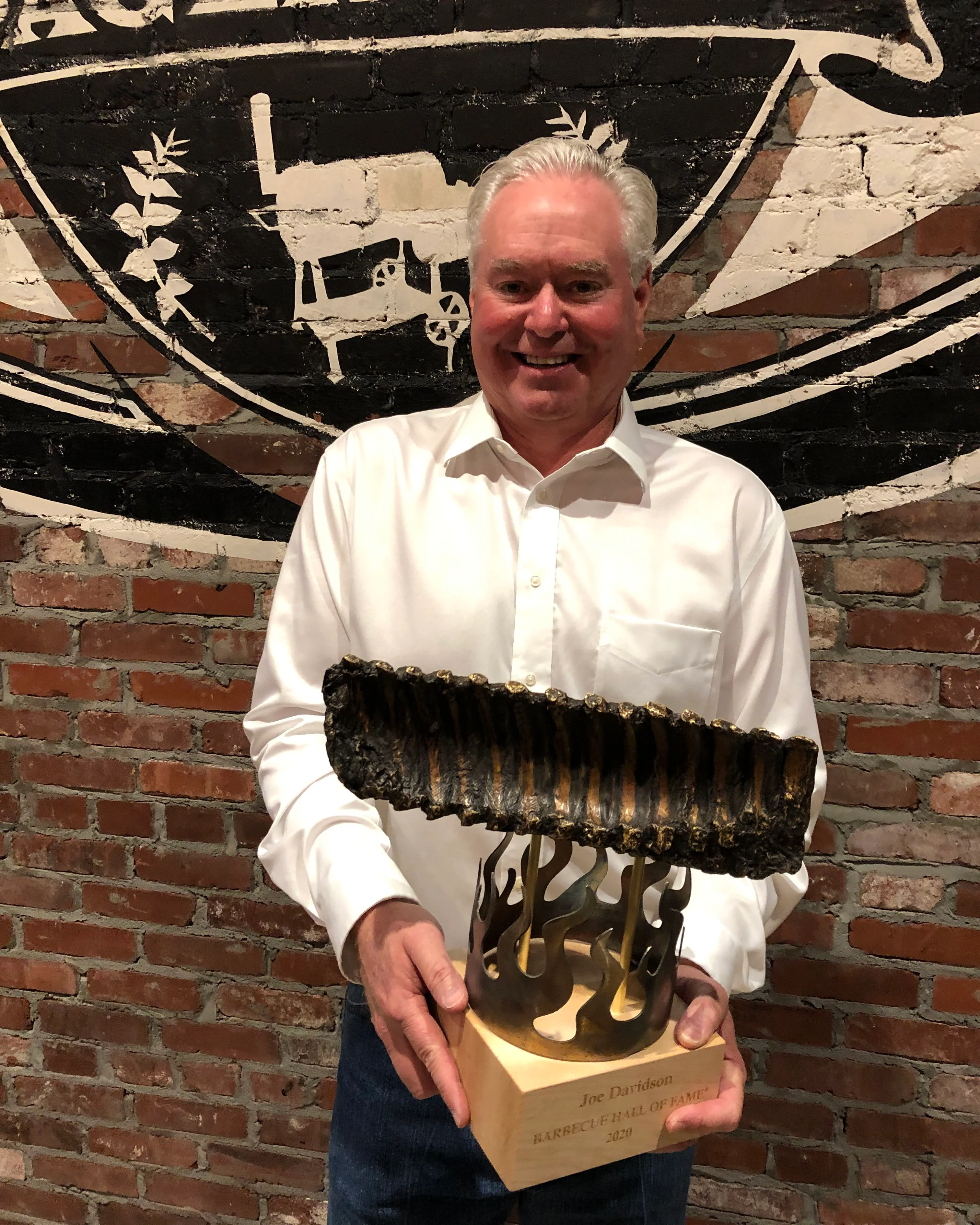 Smiling man holding a barbecue award in a rustic restaurant setting