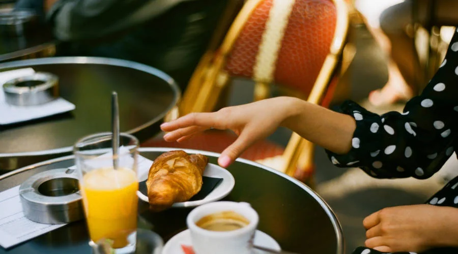 A hand reaching for a croissant on a cafe table with drinks.