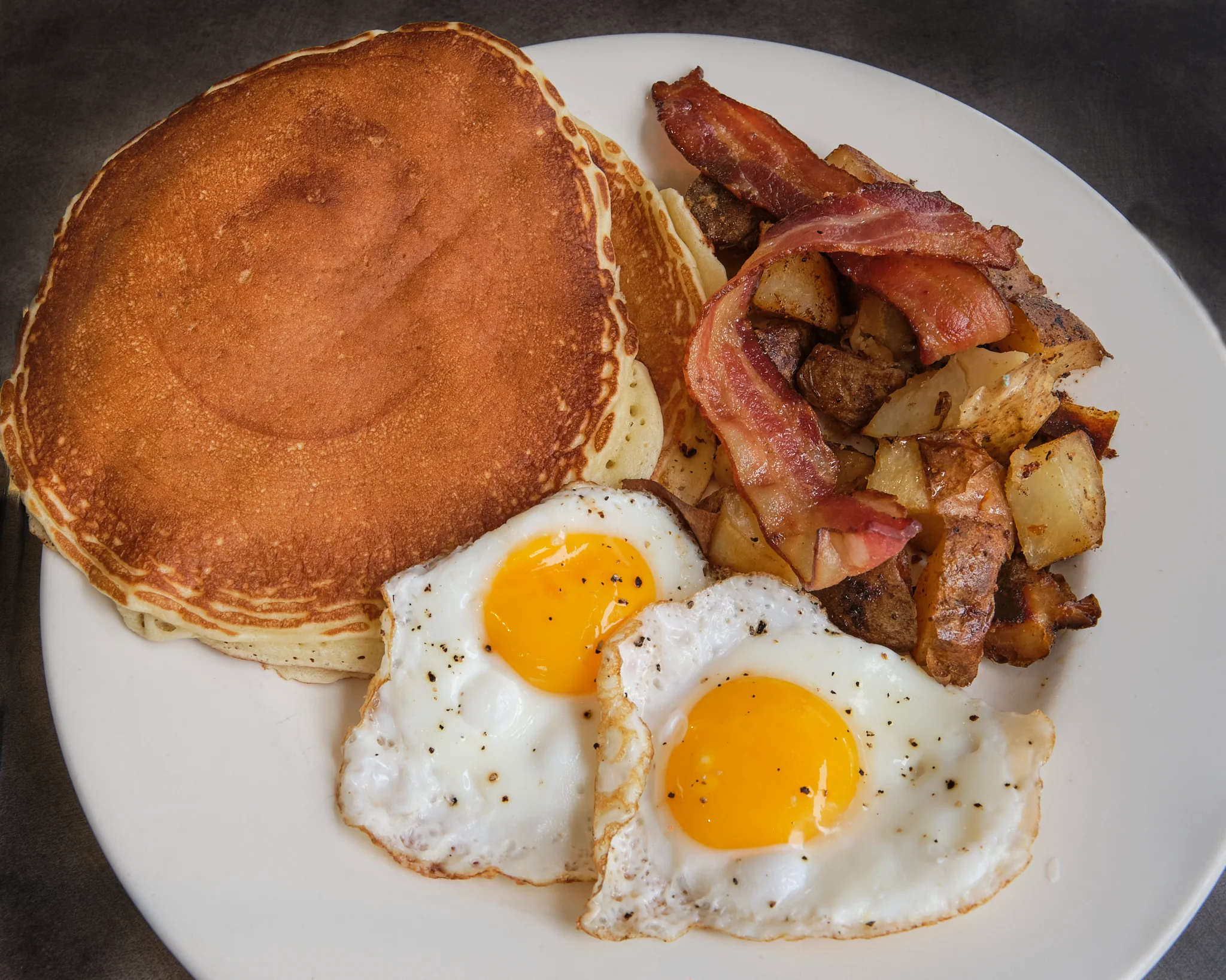 Classic American breakfast with pancakes, eggs, bacon, and potatoes