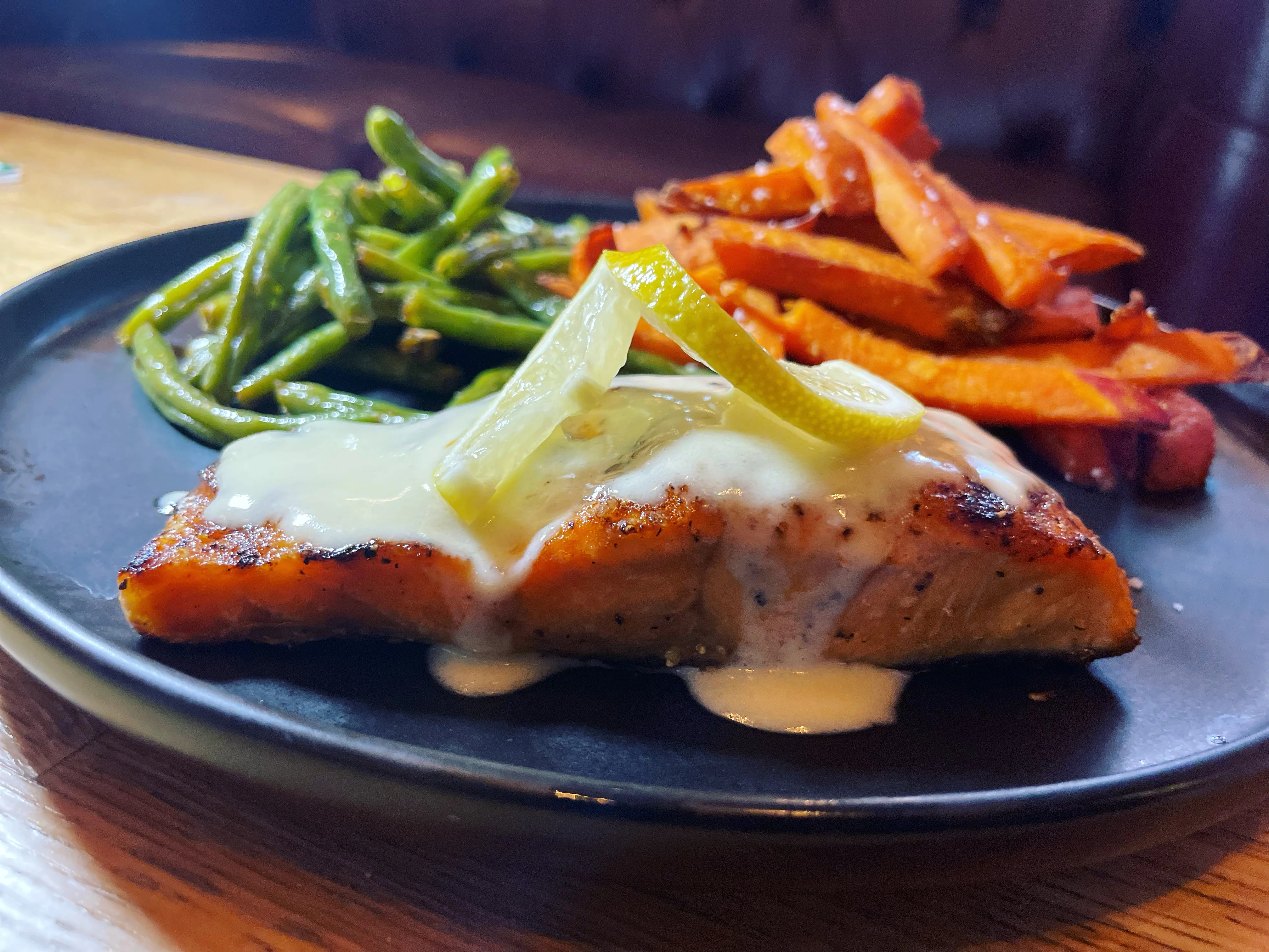 Grilled salmon with lemon sauce and sides of green beans and sweet potato fries