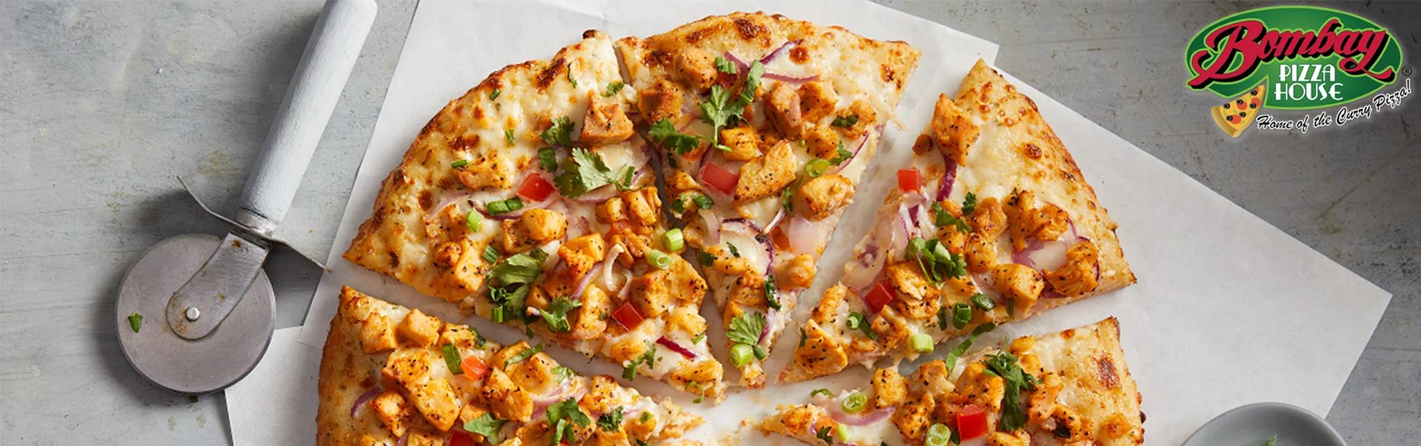 A tempting pizza featuring grilled chicken, red onions, cilantro, and a mix of vegetables, cut into slices and displayed on white parchment.