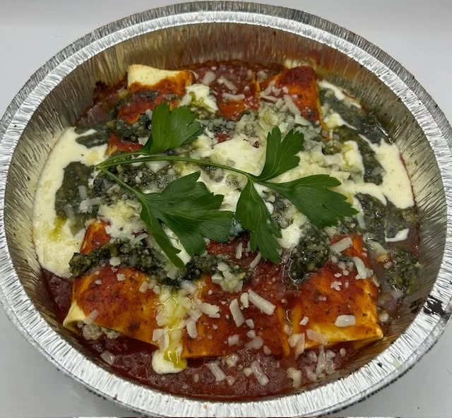 A hearty sandwich filled with meats and cheese, resting in a takeout container with messy wrappers.