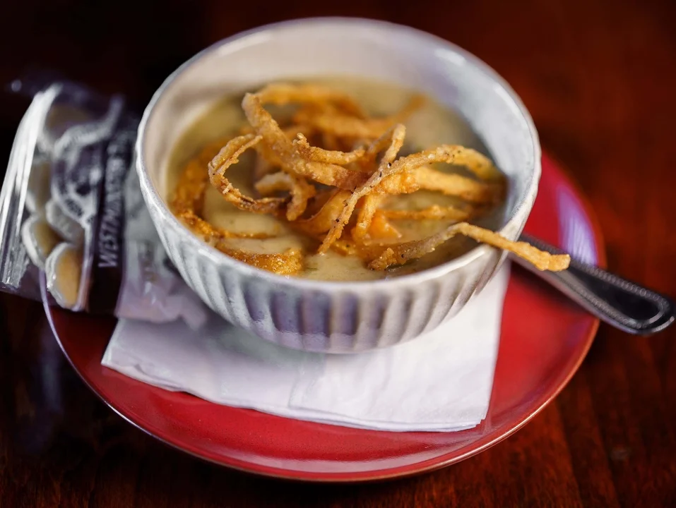 A bowl of creamy soup topped with crispy fried onions, served on a red plate with a side of crackers.