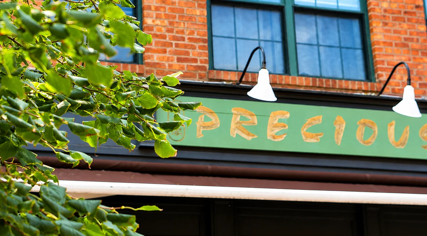 Exterior view of Precious restaurant with green signage and brick facade