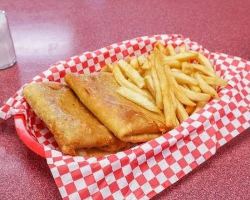 A basket filled with crispy fried items including two large pastries and a side of golden French fries, all presented on a red and white checkered paper.