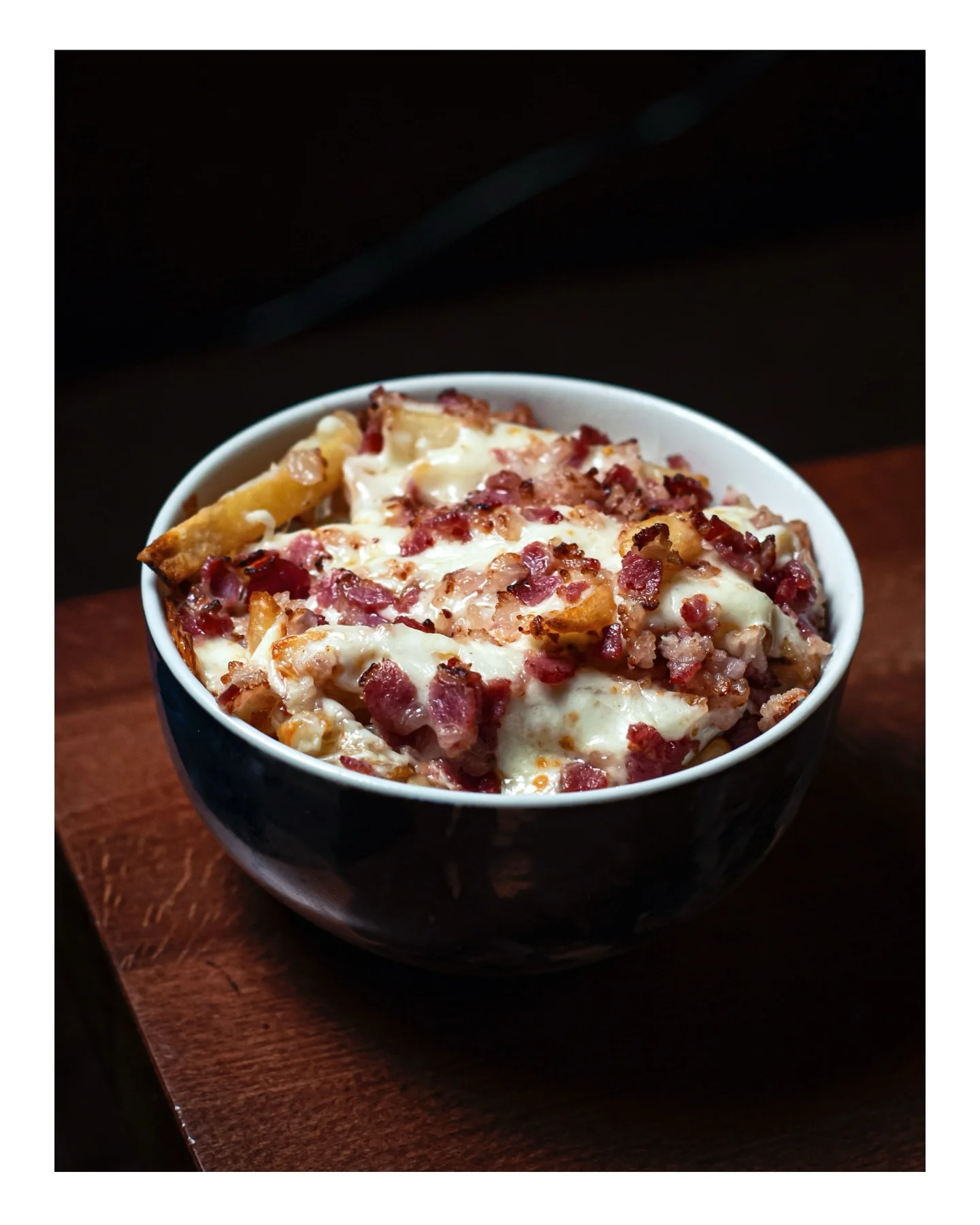 A bowl of creamy baked pasta topped with crispy bacon bits and melted cheese.