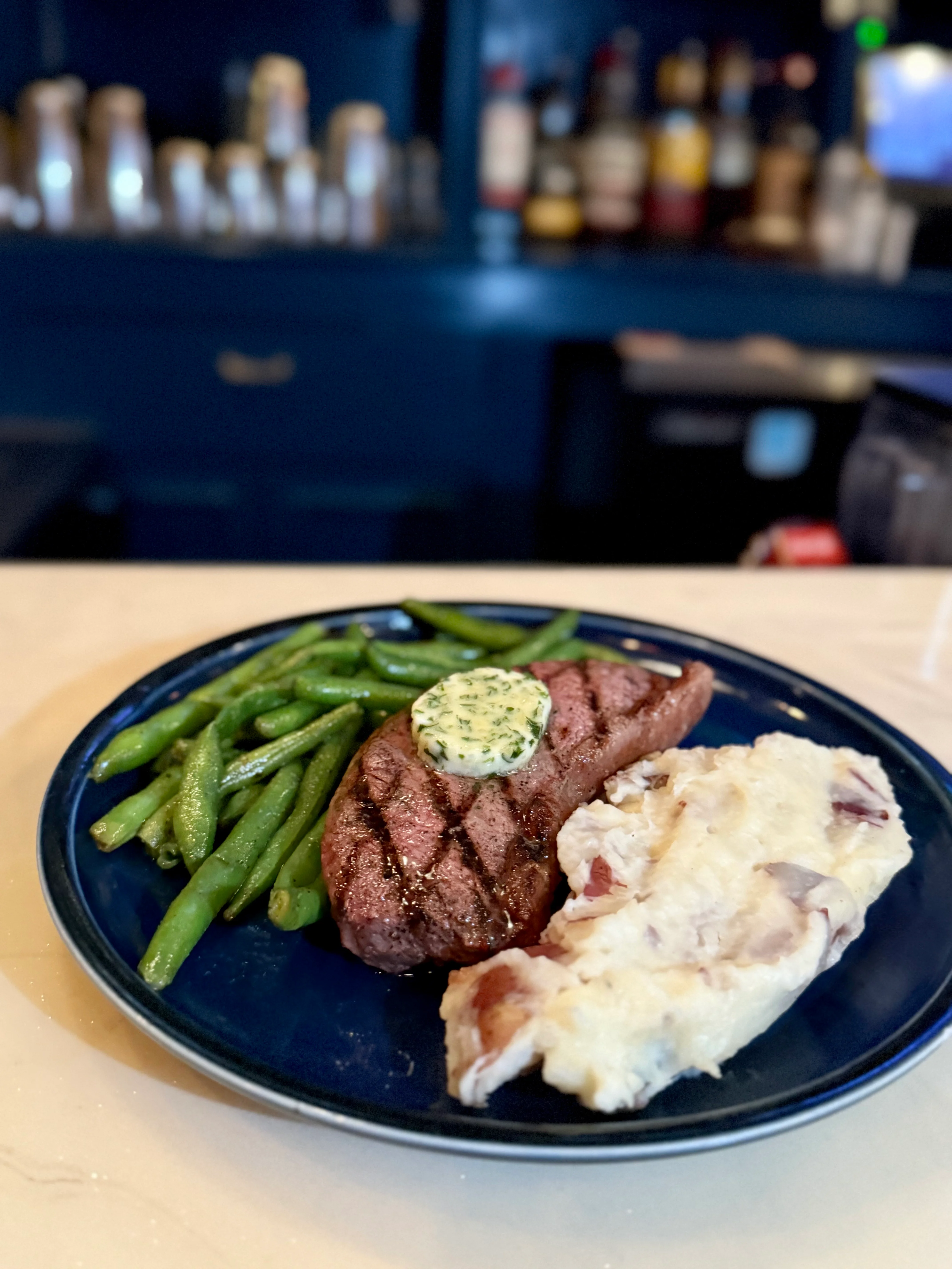 Grilled steak with herb butter, green beans, and mashed potatoes