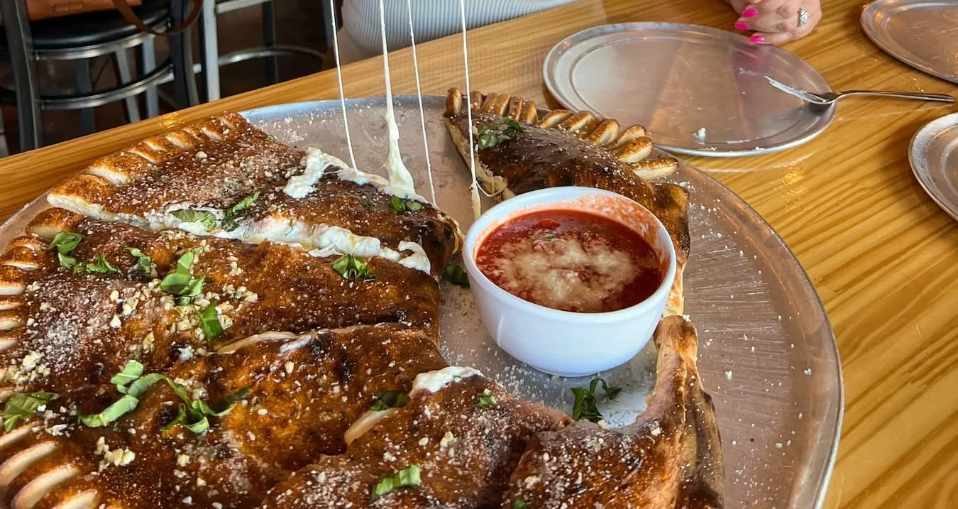 Cheesy calzone with melted cheese pulling apart, served on a plate.