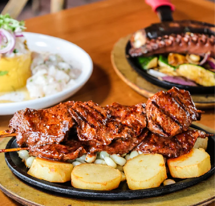 Grilled meat skewers served on a sizzling plate with potatoes.