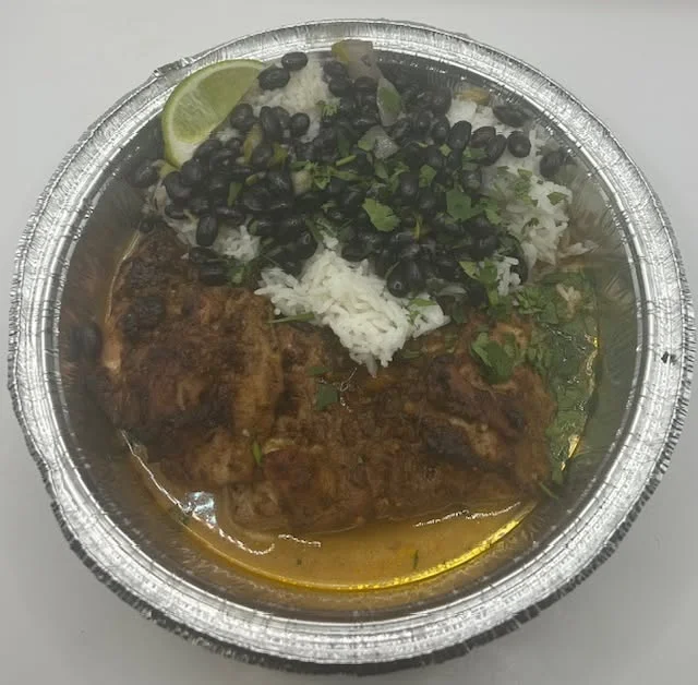 A dish featuring seasoned fish served with white rice, black beans, and fresh cilantro, garnished with a lime wedge.