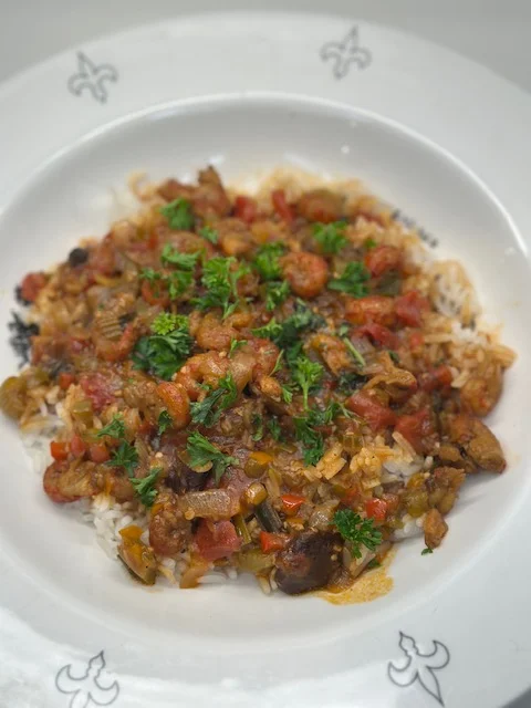 A bowl of rice topped with a mix of vegetables and shrimp, garnished with fresh parsley. The colorful dish features tomatoes and a variety of textures.