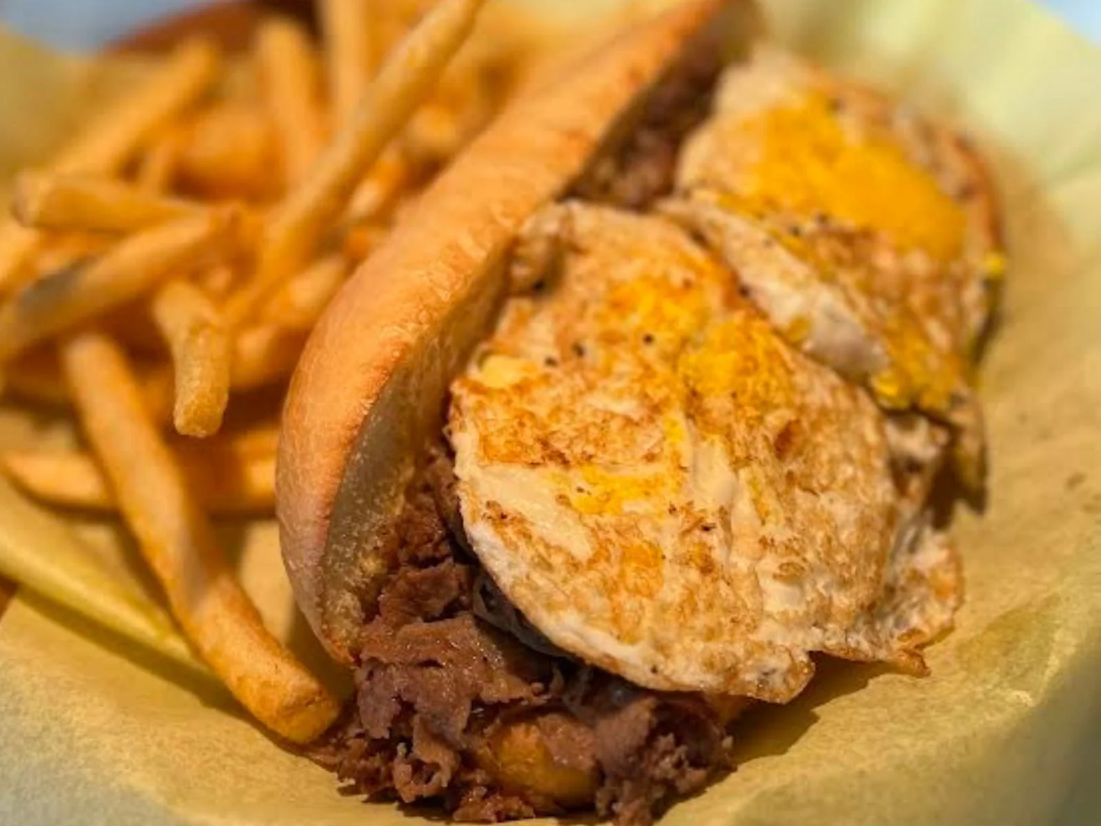Philly cheesesteak sandwich with fried eggs and fries