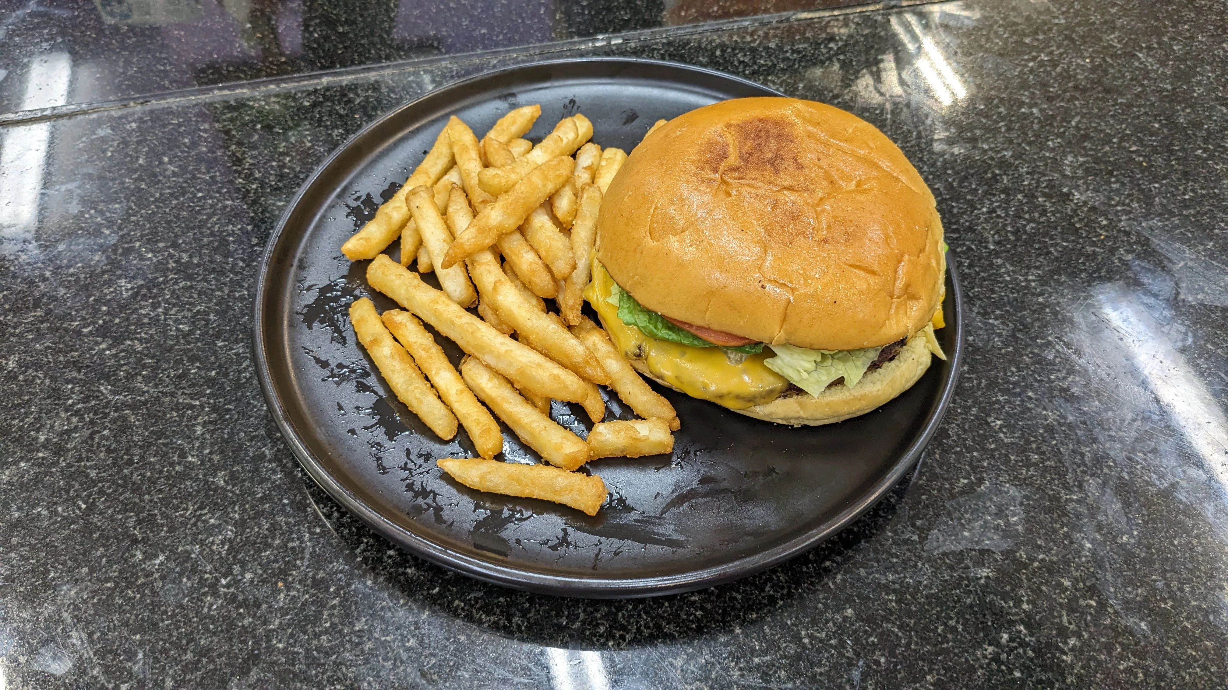 Classic American cheeseburger with fries on a black plate