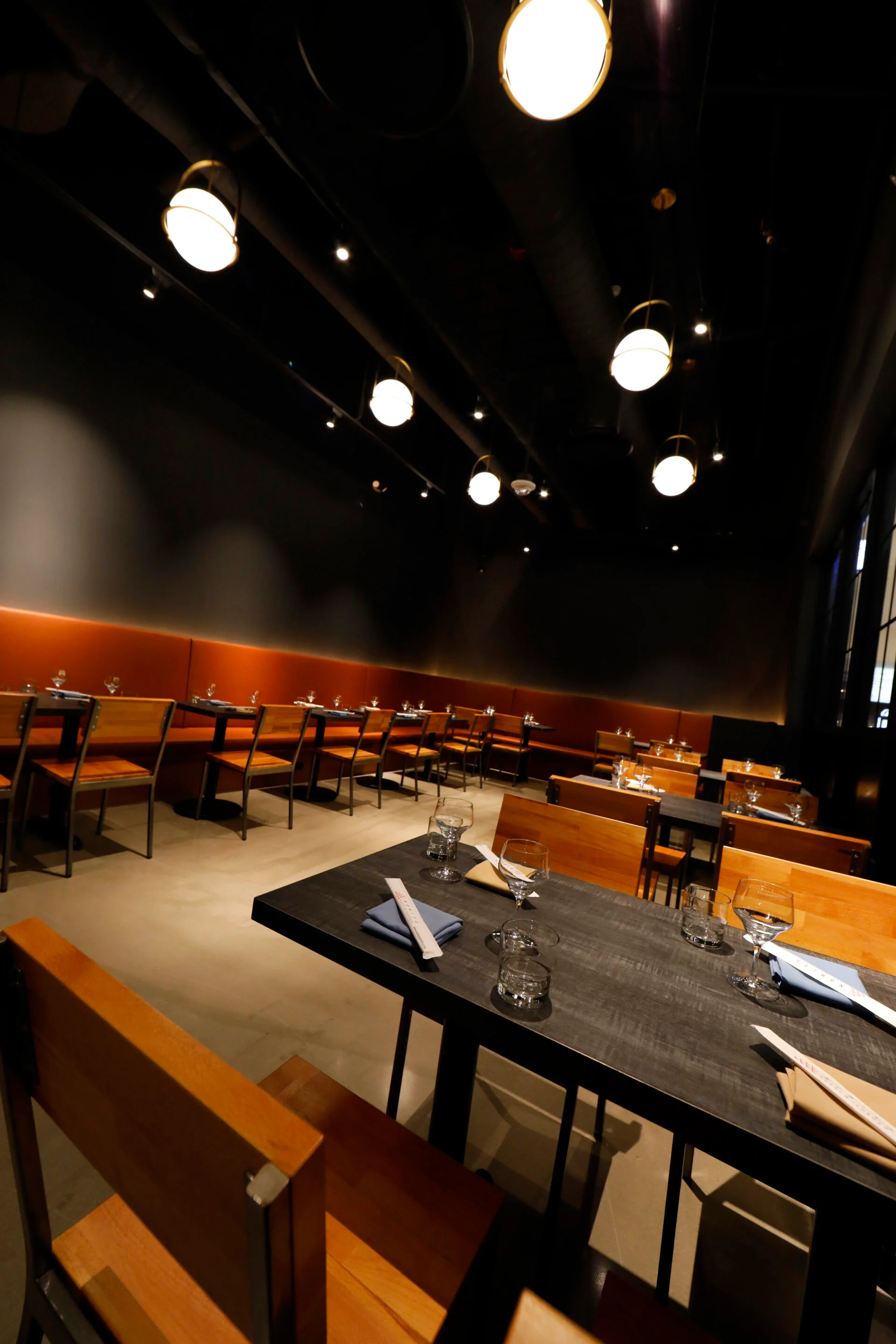 A modern dining area featuring wooden tables and metal chairs, illuminated by stylish pendant lights, creating a warm and inviting atmosphere.