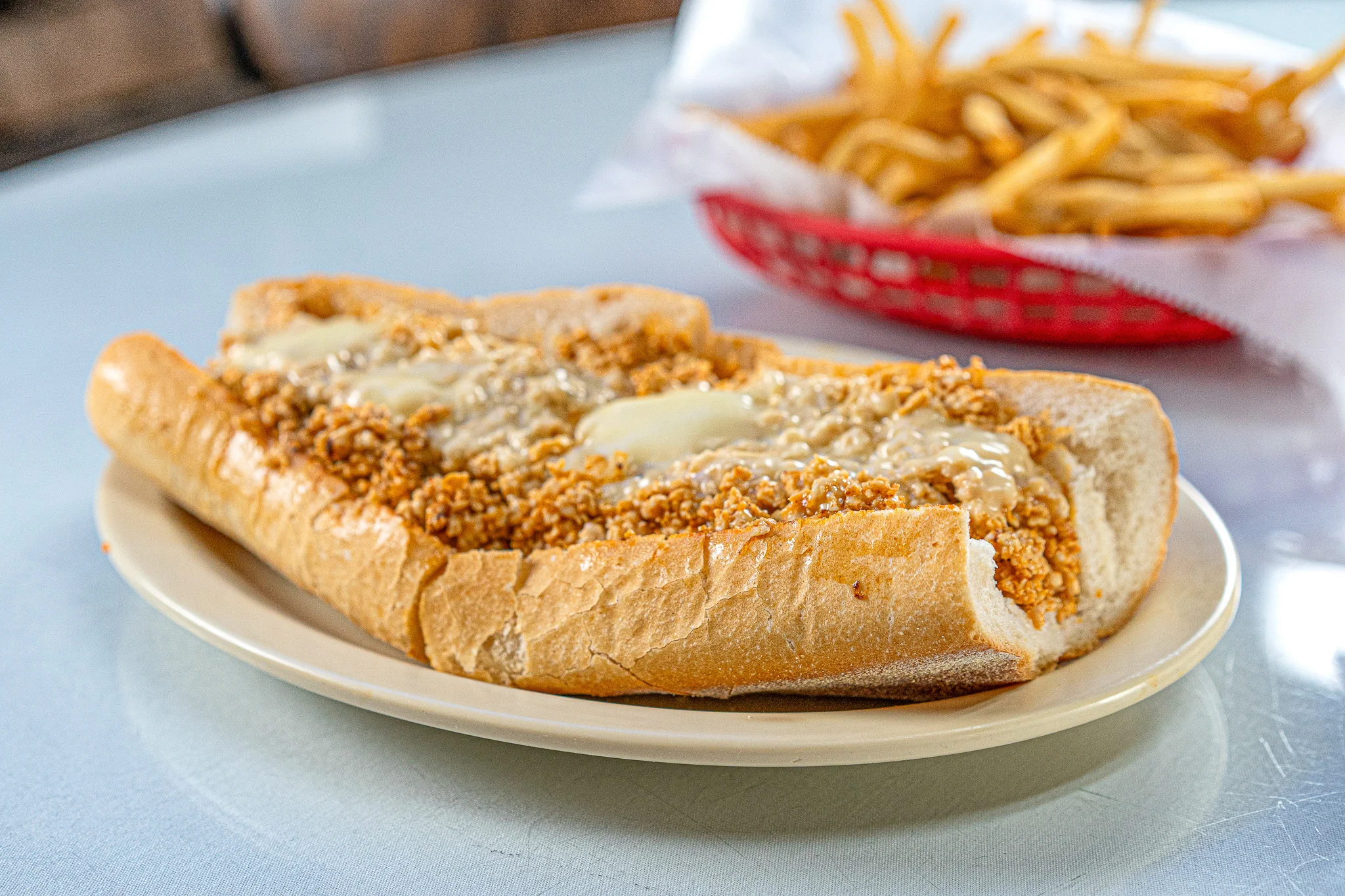 Steak Out buffalo chicken cheesesteak with melted cheese on a fresh hoagie roll, served on a white plate over blue table.