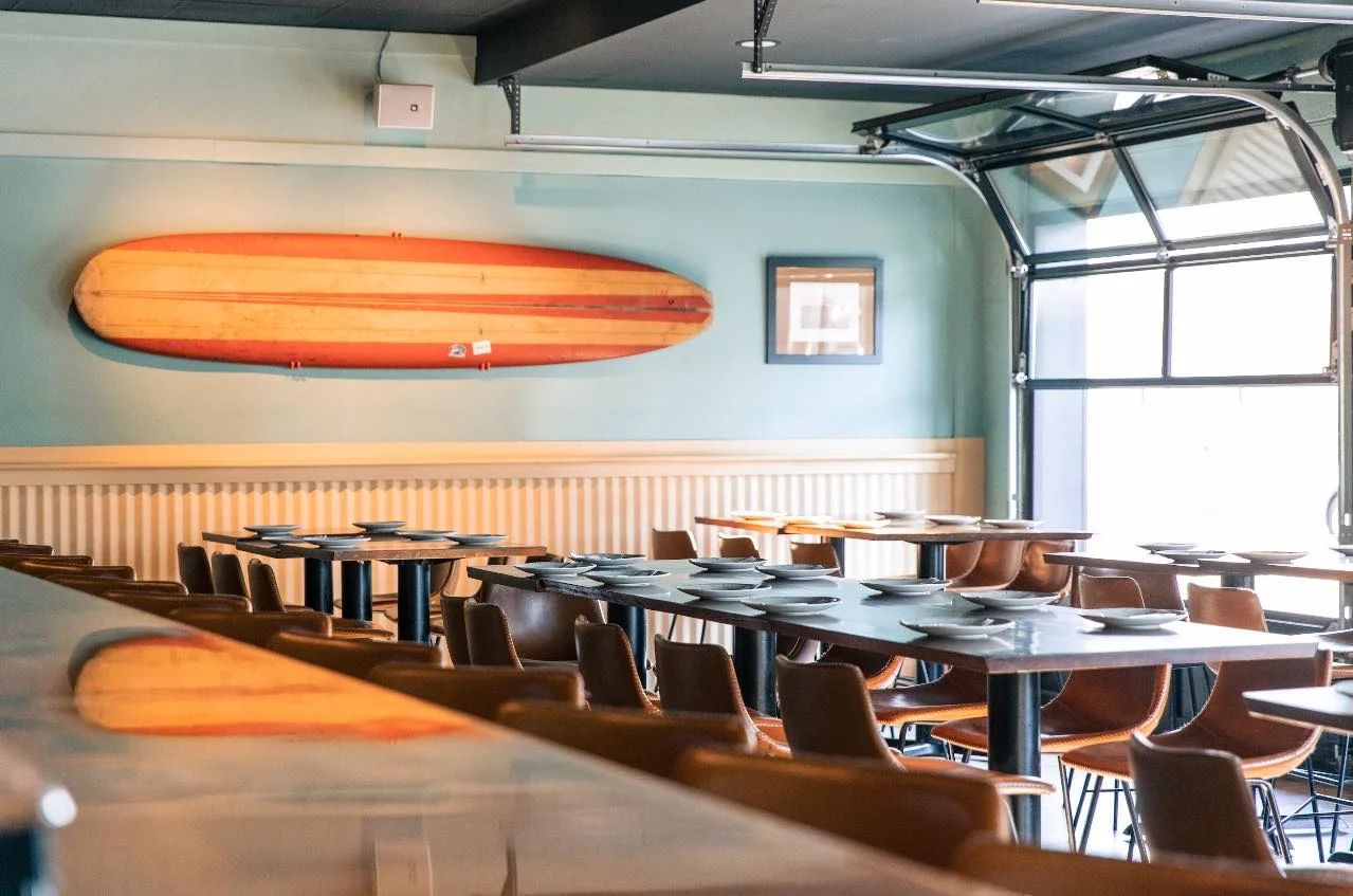Bright coastal restaurant interior with surfboard wall decor and set dining tables