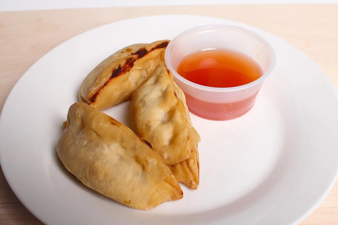 Three empanadas arranged on a plate, accompanied by a small cup of dipping sauce.