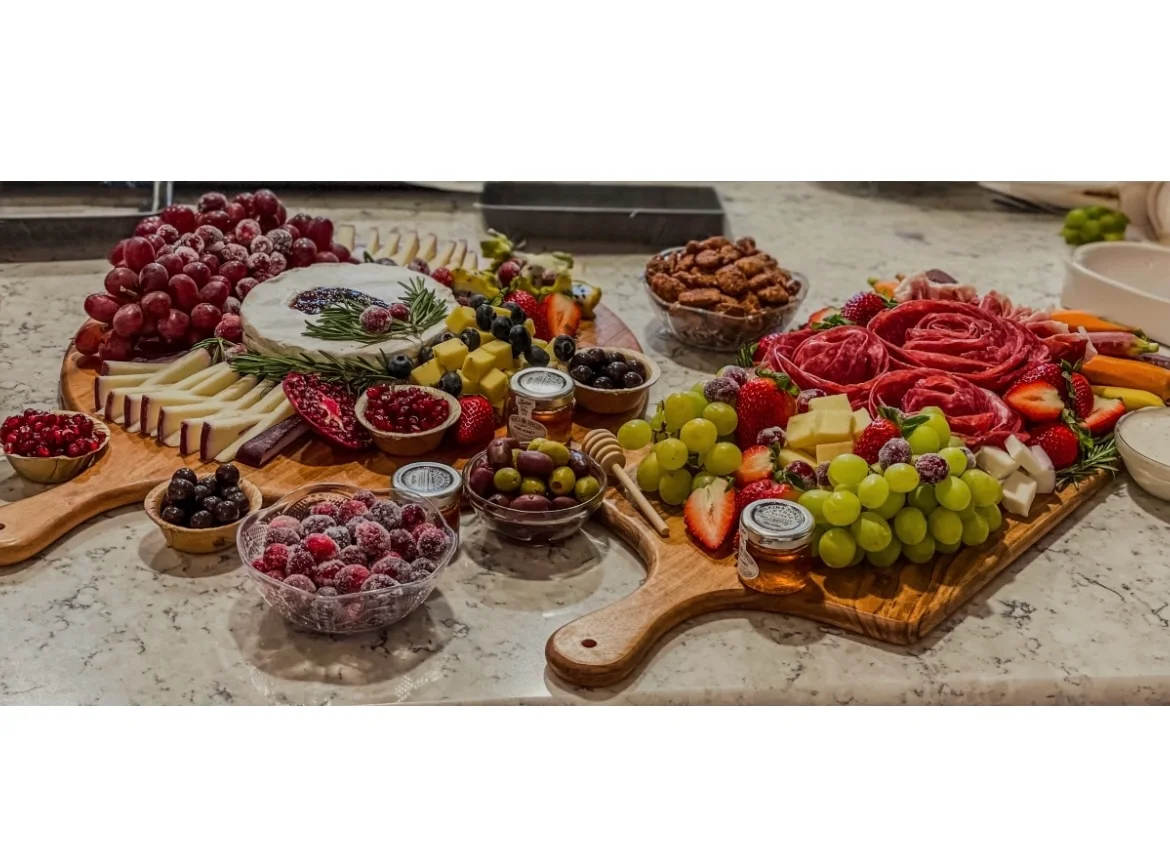 A balanced meal in a compartmentalized container featuring pasta salad with olives and peppers, a creamy spread on lettuce, assorted crackers, and a mix of fresh berries and grapes.