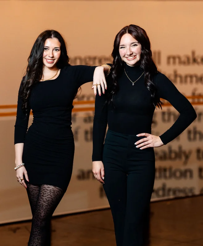 Two women posing in stylish outfits at a modern venue