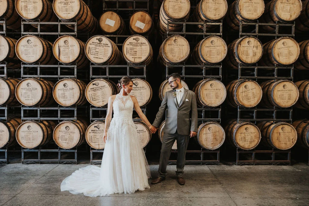 A newly married couple holding hands in front of thousands of barrels