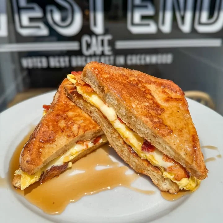 A sandwich made with grilled bread, filled with egg and bacon, drizzled with syrup.