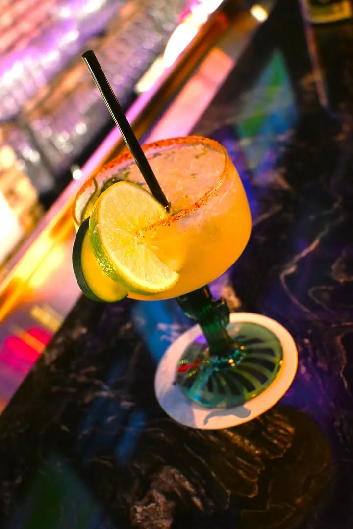 A vibrant cocktail garnished with lime slices and served in a decorative glass, sitting on a bar counter.