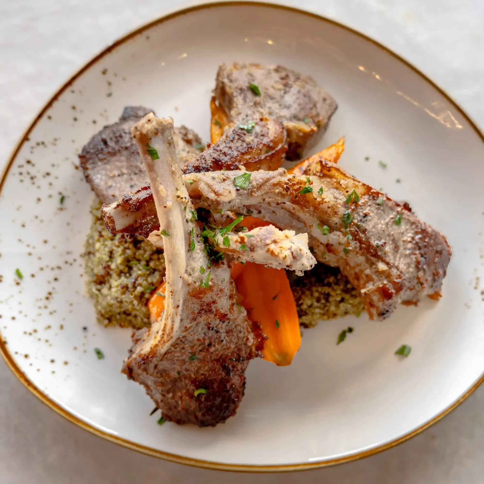 Grilled lamb chops with quinoa and roasted sweet potatoes, garnished with fresh herbs on a white plate.