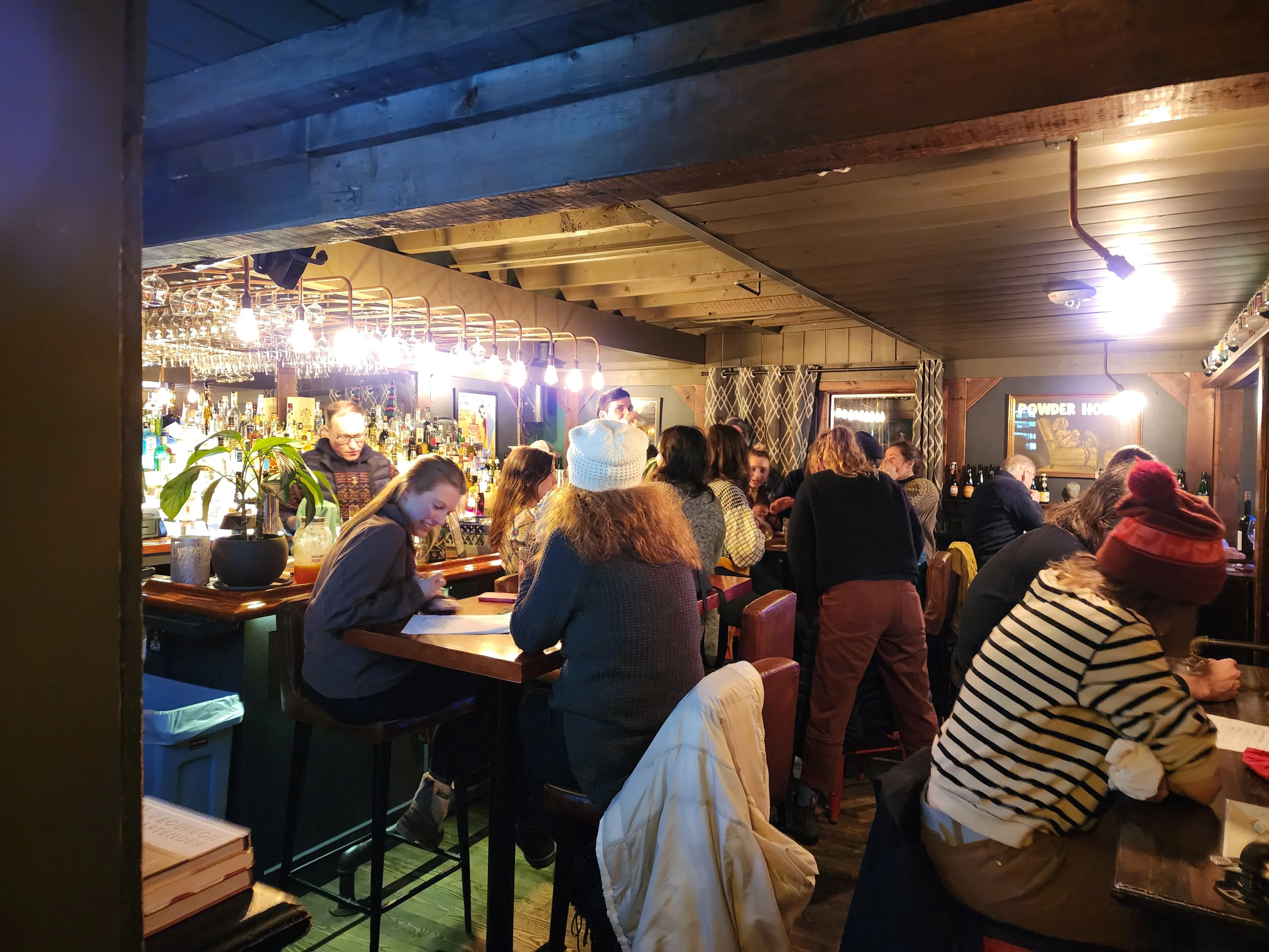 Busy restaurant bar interior with diners, exposed beams, and pendant lighting