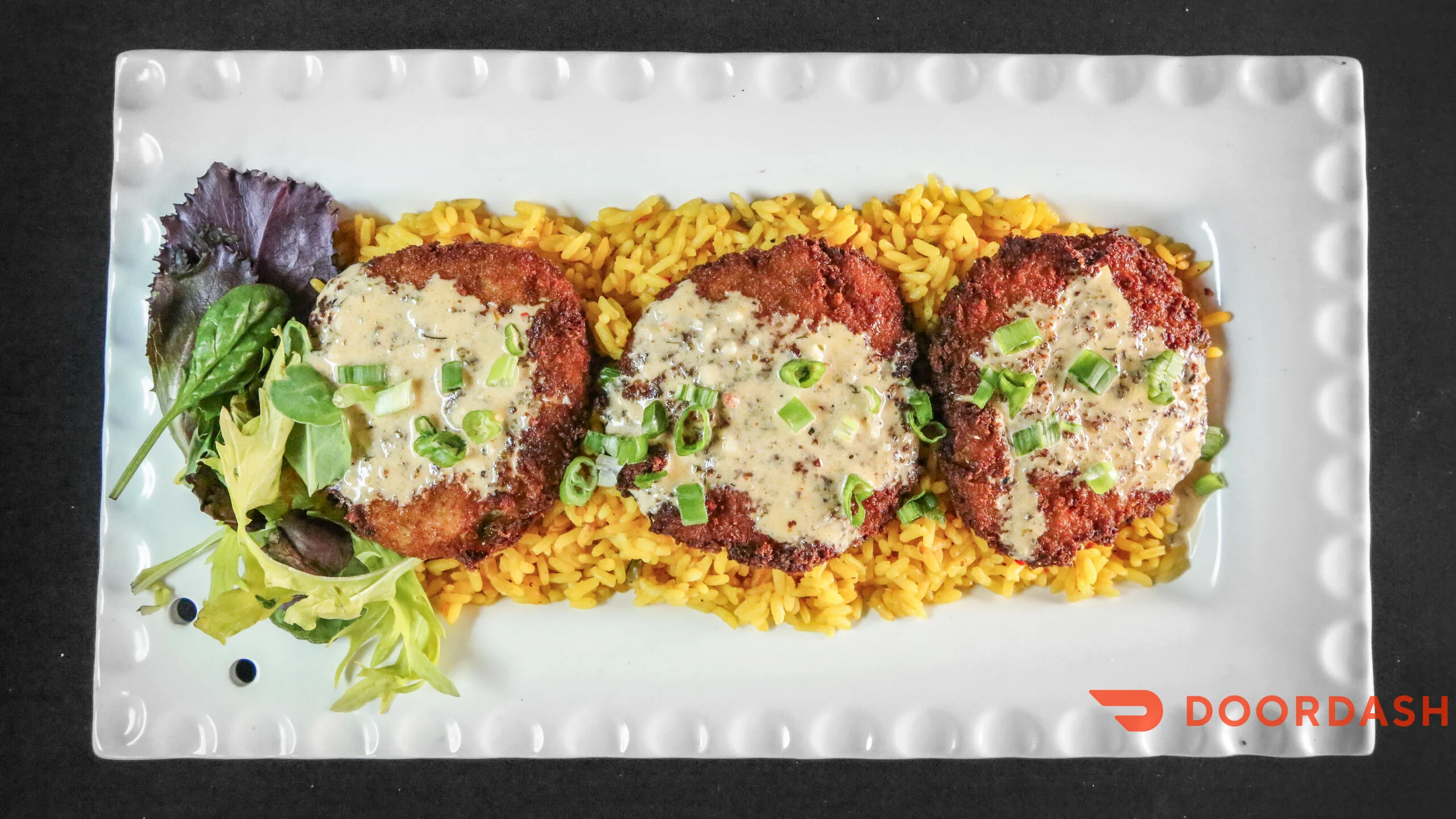 A plate featuring three crispy fried patties on a bed of yellow rice, served with a green salad.