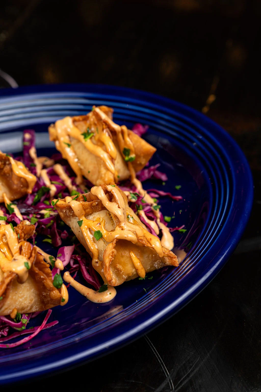 Crispy wontons drizzled with spicy sauce on a bed of purple cabbage