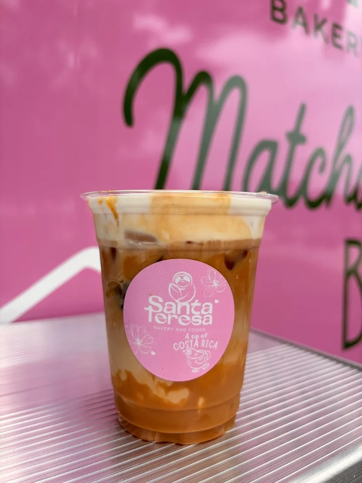 A layered iced coffee with cream and coffee combined, visible in a transparent container with a pink logo.